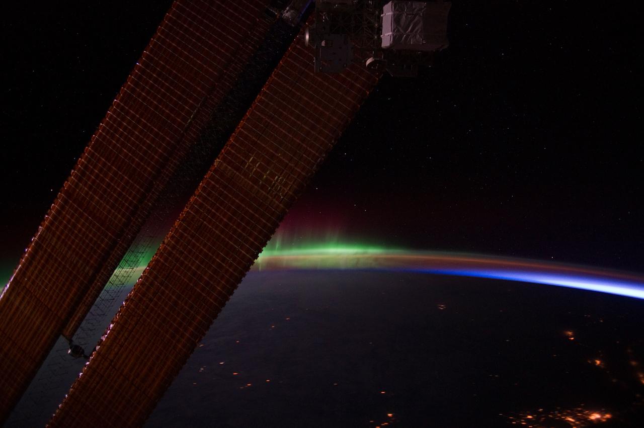 ISS030-E-075182 (4 Feb. 2012) --- This nighttime view of Earth's horizon and scattered city lights was photographed by one of the Expedition 30 crew members aboard the International Space Station. Activity of Aurora Borealis appears from behind one of the orbital outpost's solar array panels, then fades into an area where Earth's limb is visible and finally a small "slice" of daybreak appears at right.