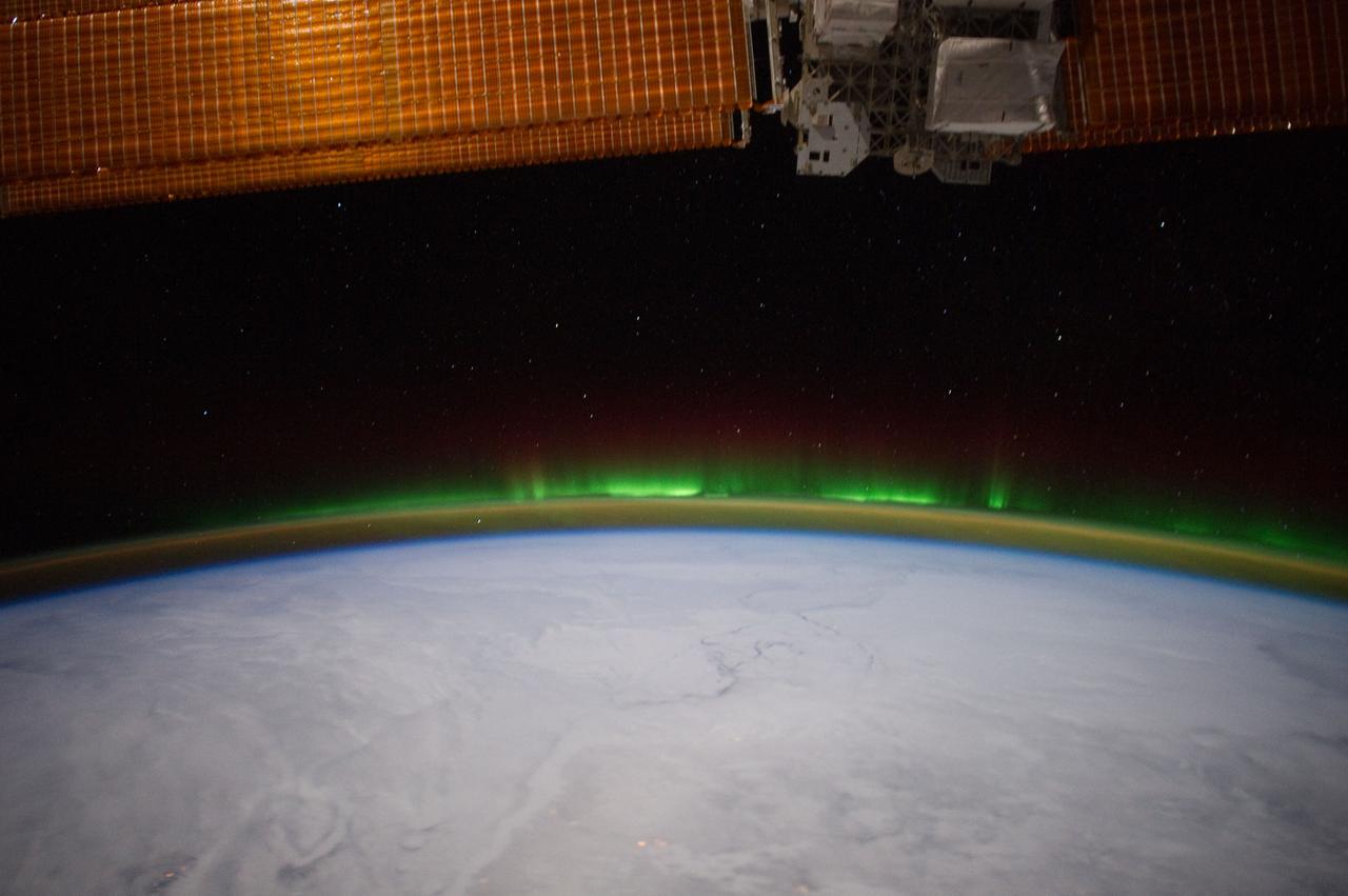 ISS030-E-114095 (6 Feb. 2012)--- Minor activity of Aurora Borealis is easily recognized "piggybacking" Earth's limb in this 24-mm image photographed by one of the Expedition 30 crew members aboard the International Space station from approximately 240 miles above Earth. Clouds obscure what would be any recognizable points on the planet.  A section of one of the solar array panels on the orbital outpost is seen across the top of the frame.
