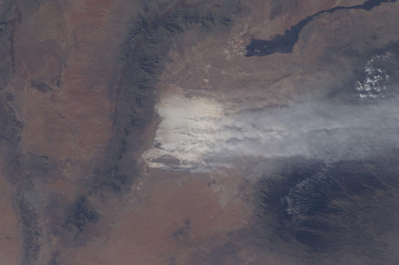 ISS030-E-174652 (28 Feb. 2012) --- A dust storm near the White Sands National Monument, New Mexico, USA is featured in this image photographed by an Expedition 30 crew member on the International Space Station. Driven by winter winds from the southwest, white dust from the White Sands dune field (center) in New Mexico rises thousands of feet from the valley floor, up and over the snowy peaks of the Sacramento Mts. downwind (right). White Sands National Monument lies in the 50 kilometers-wide Tularosa valley, between the dark rocks and forested slopes of the Sacramento Mts. and the San Andres Mts. (left center). The lower and warmer ridge line of the San Andres was without snow on this day. The striking black lava flows of the Carrizozo lava field also occupy the valley floor (top right). The darker tones of agriculture in the Rio Grande floodplain can be seen along the left margin of the image. The length of the dust plumes in this photograph is more than 120 kilometers. The vigor of the winds on this day can be judged also from the fact that they are lifting the dust particles from the valley floor more than 1,200 meters over the mountains. Winds channel the dust through a low point on the Sacramento Mts., some 800 meters below the ridge crests to north and south (right). The Moderate Resolution Imaging Spectroradiometer (MODIS) on the NASA Aqua satellite also captured a wider regional view of the extent of the plumes on the same day. In most parts of the world blowing dust is some shade of light brown or red.  It is interesting to observe two colors of dust that contribute to this dust plume: redder dust from the local hillsides north of White Sands (seen by the small brown zone along the northern margin of the dust mass), and the white dust from the dune field. The sand dunes of the Monument are white since they are composed of the mineral gypsum, a relatively rare dune-forming mineral. The gypsum is deposited during evaporation of mineral-rich waters in an ephemeral lake located in the western part of the Monument. Erosion of the deposits, together with wind transport, provides the granular material for the dunes. The dunes? brilliance, especially contrasted against the nearby dark mountain slopes, makes the dunes easily identifiable at great distances by orbiting astronauts. The white speck of the dunes is even visible in images taken looking back at Earth by crews on the way to the moon.