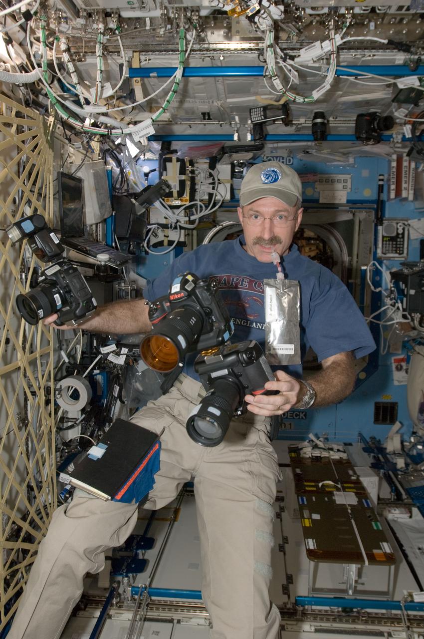 ISS030-E-175780 (15 Jan. 2012) --- NASA astronaut Dan Burbank, Expedition 30 commander, is pictured with still cameras and a punch beverage in the Destiny laboratory of the International Space Station. Two of the cameras are mounted together; one being an infrared modified still camera.