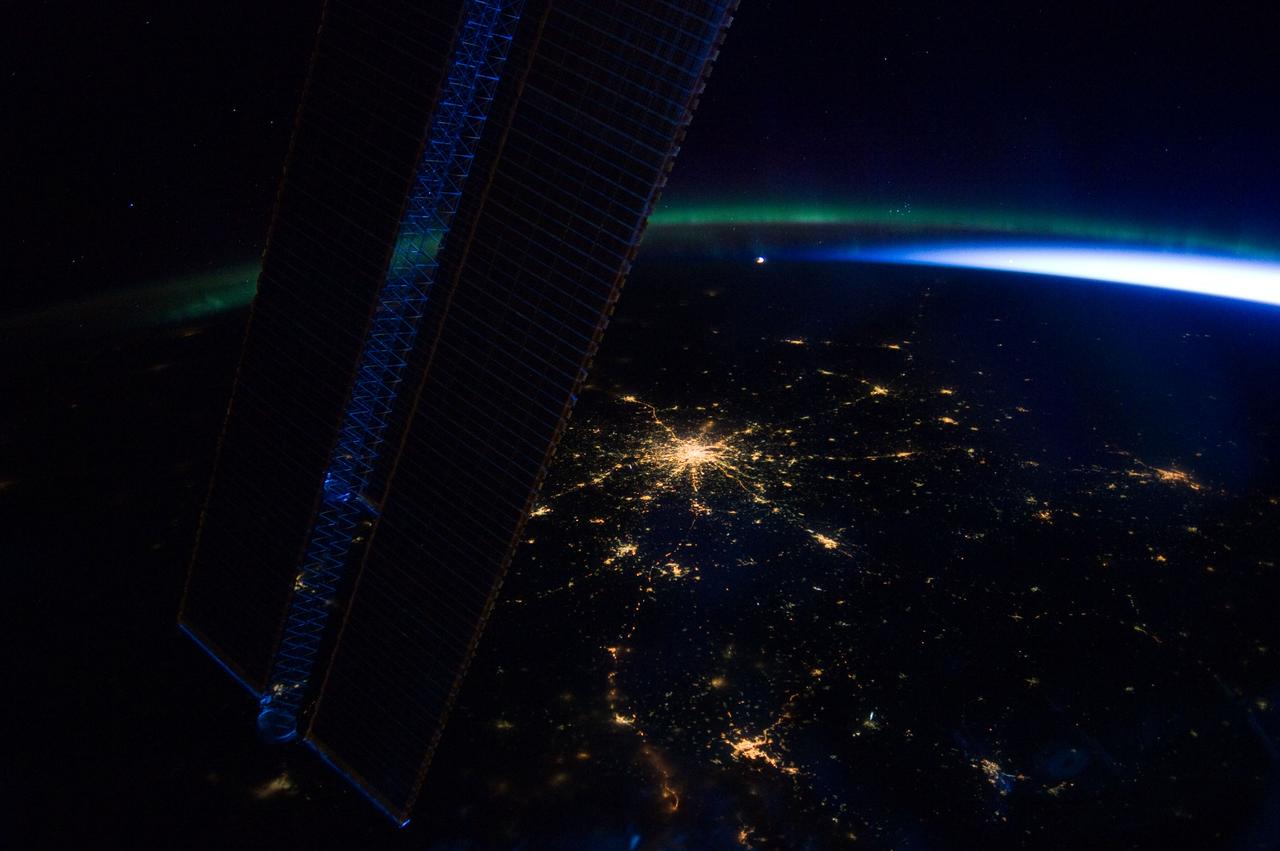 ISS030-E-185327 (28 March 2012) --- Moscow, Russia appears at the center of this nighttime image photographed by one of the Expedition 30 crew members aboard the International Space Station, flying at an altitude of approximately 240 miles. A solar array panel for the space station is on the left side of the frame. The view is to the north-northwest from a nadir of approximately 49.4 degrees north latitude and 42.1 degrees east longitude, about 100 miles west-northwest of Volgograd. On the horizon in the background can be seen a small sample of Aurora Borealis, airglow and daybreak.