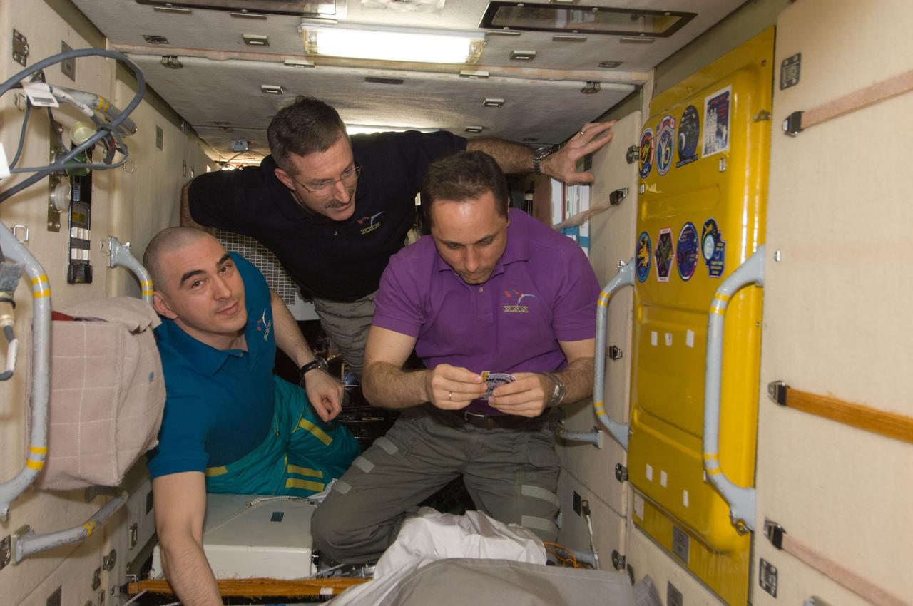 ISS030-E-241363 (21 April 2012) --- In the Zarya Functional Cargo Block (FGB), NASA astronaut Dan Burbank (center), Expedition 30 commander; along with Russian cosmonauts Anton Shkaplerov (right) and Anatoly Ivanishin, both flight engineers, prepare to add the Soyuz TMA-22 patch to the growing collection of insignias representing crews who have worked on the International Space Station.