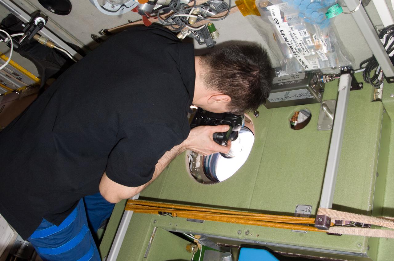 ISS031-E-005810 (27 April 2012) --- Russian cosmonaut Oleg Kononenko, Expedition 31 commander, uses a still camera at a window in the Zvezda Service Module of the International Space Station to photograph the departure of the Soyuz TMA-22 spacecraft carrying Expedition 30 crew members back to Earth.