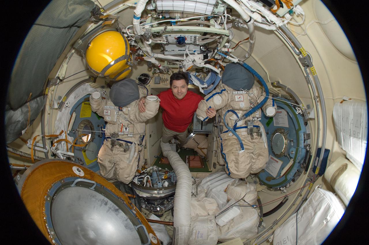 ISS031-E-030470 (12 May 2012) --- A fisheye lens attached to an electronic still camera was used to capture this image of Russian cosmonaut Oleg Kononenko, Expedition 31 commander, with two Russian Orlan spacesuits in the Pirs Docking Compartment of the International Space Station.