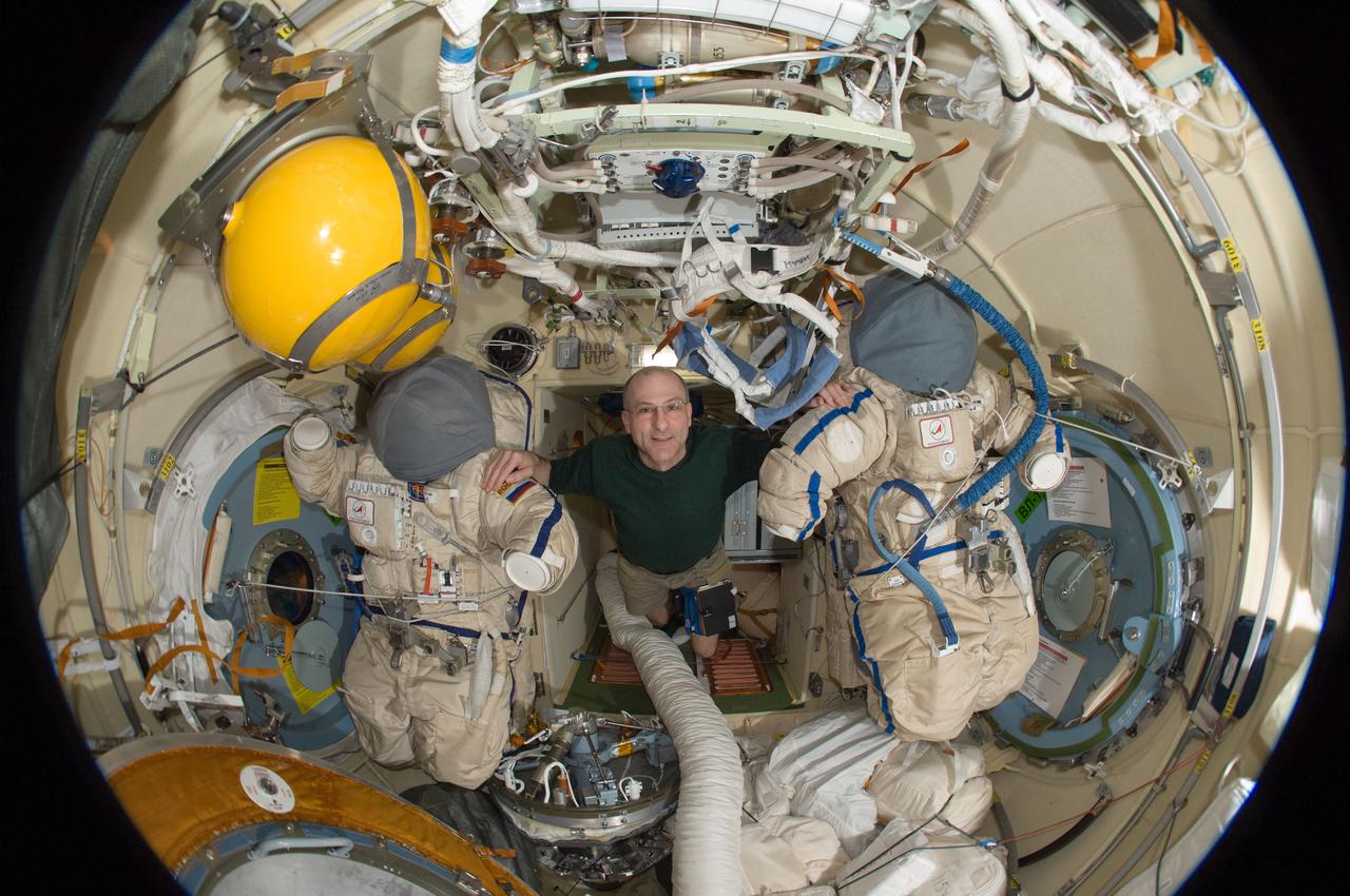 ISS031-E-030471 (12 May 2012) --- A fisheye lens attached to an electronic still camera was used to capture this image of NASA astronaut Don Pettit, Expedition 31 flight engineer, with two Russian Orlan spacesuits in the Pirs Docking Compartment of the International Space Station.