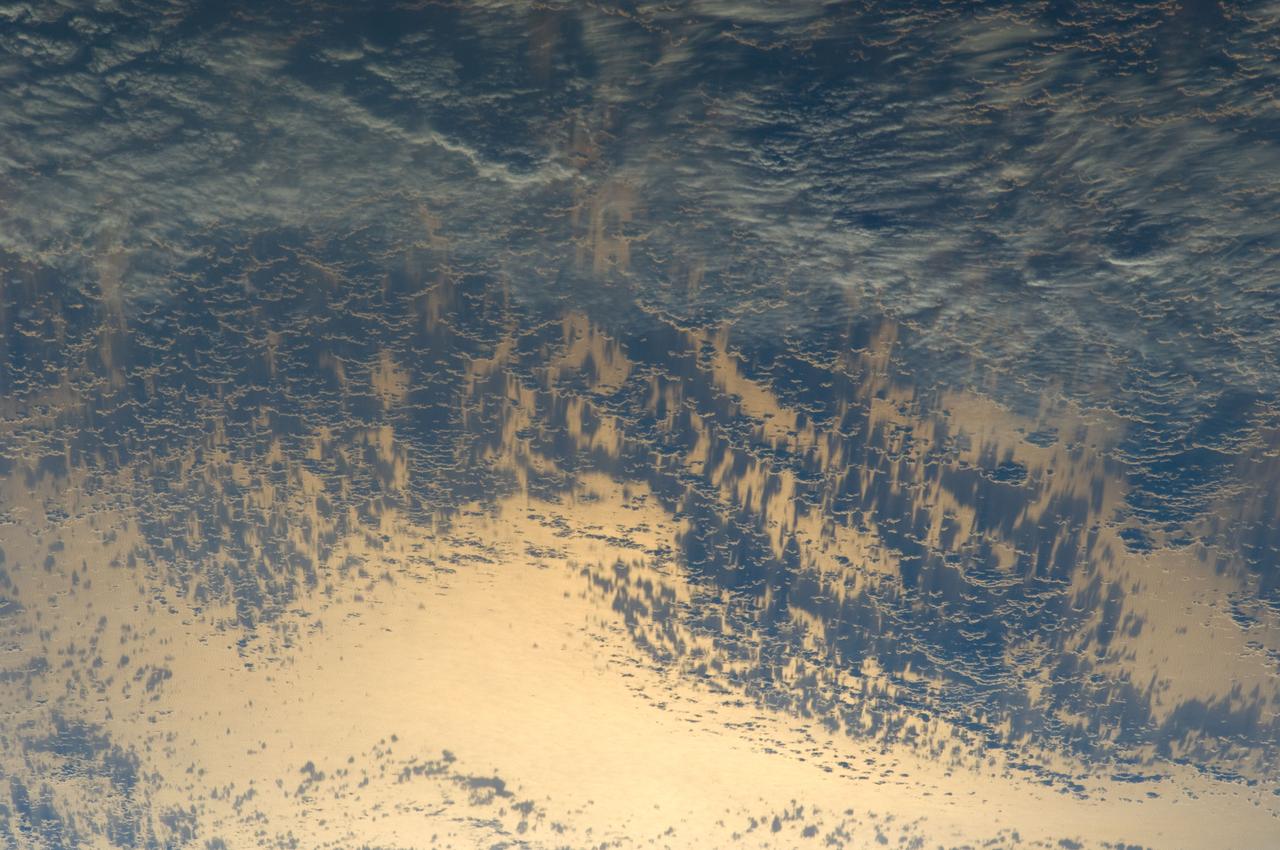 ISS031-E-035310 (15 May 2012) --- Sunglint and clouds off Western South America are featured in this image photographed by an Expedition 31 crew member on the International Space Station. The setting sun highlights cloud patterns above the Pacific Ocean, as well as the ocean surface itself in this impressive image. The space station was located over the Andes Mountains of central Chile at the time. The view is looking towards the Pacific Ocean and the sun setting in the west (towards lower left). Light from the setting sun reflects off the water surface towards the observer on the space station and creates a mirror-like appearance—a phenomenon known as sunglint. Bands of relatively low altitude cumulus clouds appear much like a flotilla of ships with their west-facing sides illuminated by the waning sunlight and the rest in shadow (center). Due to the low sun angle, they cast long and deep shadows over large swaths of the ocean surface. Given the short camera lens used, an individual cloud shadow may extend for miles. Light gray clouds at upper right appear to be at a higher altitude. The cloud cover is likely a remnant of a frontal system that moved inland over South America from the Pacific a day or two prior to the time the image was taken.