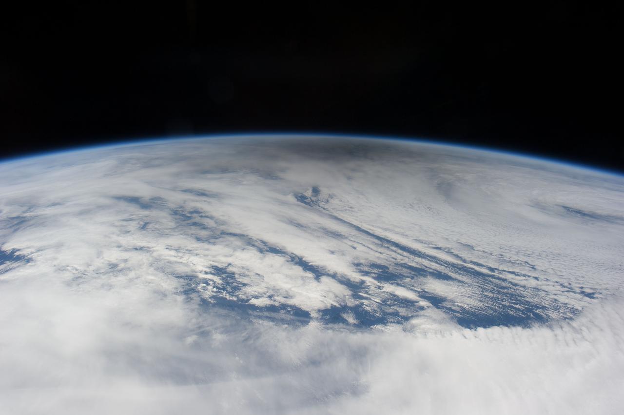 ISS031-E-041657 (20 May 2012) --- Photographed by the Expedition 31 crew aboard the International Space Station and easily spotted at top center in this image is the smoky gray shadow of the moon, cast on bright clouds of the northern Pacific Ocean. The eclipse is seen obliquely, with its center more than 1600 kilometers away, so it appears as a flattened circle. Images taken three minutes earlier near the point of closest approach (slightly more than 600 kilometers) to the track of the eclipse, show the shadow as a rounder shape. The crew onboard the station looked due north towards the Aleutian Islands, where the solar eclipse was near total. Twenty-three minutes later, as they approached Antarctica in the other hemisphere, the crew members saw the sun set as they passed onto the dark side of the planet. The edge of the shadow looks diffused because of the partial eclipse zone—the wide area where more or less of the sun can be seen around the edge of the moon. The zone of partial eclipse covers a far wider area than the area covered by the total eclipse.