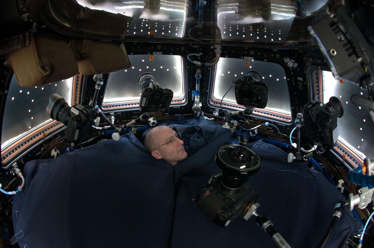ISS031-E-112289 --- Astronaut Don Pettit, Expedition 31 flight engineer, in a special "tent" fashioned to limit light in Cupola, is surround by a battery of stationary cameras.