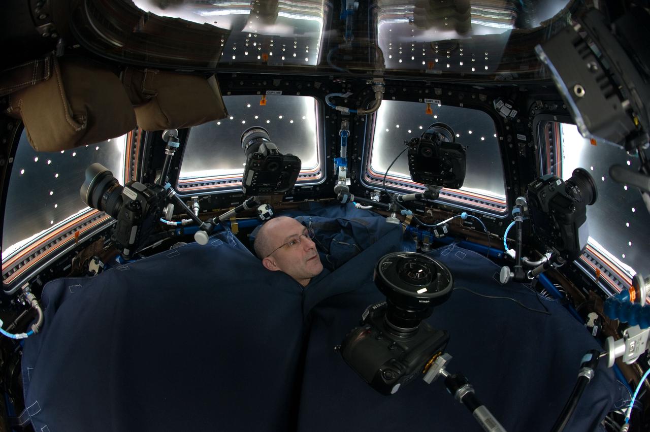 Expedition 31 flight engineer Don Pettit, with only his head visible above a shroud, is photographed in the Cupola Module. Window shutters are closed, and still cameras are positioned in front of each window