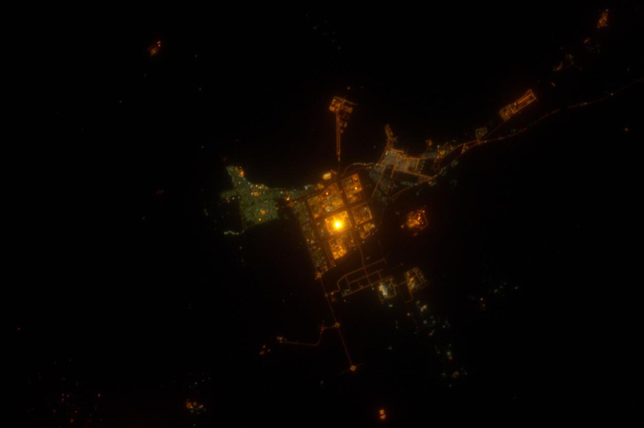 ISS031-E-143143 (19 June 2012) --- Al Jubayl, Saudi Arabia at night is featured in this image photographed by an Expedition 31 crew member on the International Space Station. The city of Al Jubayl (or Jubail) is located on the Saudi Arabian coastline of the Persian Gulf. The city has a history extending back more than 7,000 years, but since 1975 it has been associated with the heavy industries of petrochemical refining and production, fertilizer production and steel works. At night, these industrial areas form a brightly lit region (center) to the south of the residential and commercial center of Al Jubayl (characterized by green-gray lighting). An artificial peninsula extending into the Persian Gulf to the northeast hosts supertanker docks and petroleum storage facilities. The Persian Gulf to the north and northeast is devoid of lights; likewise, the open desert to the south-southeast provides a stark contrast to the well-lit urban and industrial areas. A bright circle of light located within the heavy industrial area (center) cannot be resolved in this photograph, but is likely a concentration of lights associated with ongoing processing or construction activities. The approximate scale of the feature ? hundreds of meters in diameter ? is consistent with multiple stationary light sources, particularly if the light from those sources is accentuated due to the camera?s low light settings.