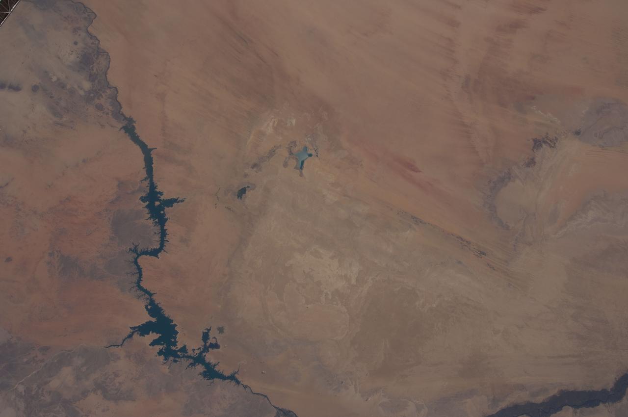 ISS031-E-148455 (21 June 2012) --- Toshka Lakes in southern Egypt are featured in this image photographed by an Expedition 31 crew member on the International Space Station. The Toshka Lakes (center) were formed in the Sahara Desert of Egypt by water from the River Nile conveyed from Lake Nasser by a canal to the Toshka Depression. Flooding of the Toshka Depression had created the four main lakes with a maximum surface area in 2002 of approximately 1,450 square kilometers ? around 25.26 billion cubic meters of water. By 2006 the stored water was reduced by 50 per cent and by 2012 shows open water only in the lowest parts of the main western and eastern basins?representing a reduction in surface area to 307 square kilometers?nearly 80 per cent smaller than the 2002 surface area. Standing water is almost completely absent from the central basin. From space, astronauts documented the first lake?the easternmost one?in 1998. The lakes progressively grew in depressions to the west, the westernmost filling between 2000 and 2001. This image shows lines of center-point agricultural fields near the east-basin lake nearest Lake Nasser. Sunglint on the western lake makes the water surface appear both light and dark, depending on which parts of the surface were ruffled by the wind at the moment the image was taken.