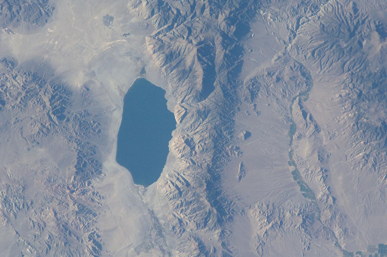 ISS032-E-010487 (29 July 2012) --- Walker Lake, Nevada is featured in this image photographed by an Expedition 32 crew member on the International Space Station. According to scientists, the Pleistocene landscape of western Nevada approximately 15,000 years ago was one of narrow mountain ranges and numerous interconnected lakes that together formed the extensive glacial Lake Lahontan. Scientists believe drying and warming of the regional climate since the last Ice Age led to the disappearance of the glaciers feeding meltwater to Lake Lahontan, and eventual disappearance of the lake itself. Today, few remnants of Lahontan remain; most of its arms have become dry enclosed basins known as playas. This photograph highlights Walker Lake, one of only two remnant lakes that contain water throughout the year (Pyramid Lake in Nevada is the other). The lake is located in an enclosed basin bounded by the Wassuk Range to the west and the Gillis Range to the east. It is fed by the Walker River flowing from the north. The current dimensions of the lake are approximately 21 kilometers north-south by 9 kilometers east-west. Shoreline deposits at higher elevations than the current lake level form concentric bands that are just visible in the image (bottom center) ? these record varying lake levels in the geologic past. The nearest town is Hawthorne, Nevada to the southeast. To the southwest the highest peak of the Wassuk Range, Mount Grant (elevation 3,496 meters above sea level), dominates the skyline. Green agricultural fields, primarily alfalfa, located to the west of the Wassuk Range (lower right) provide a striking contrast to the surrounding Great Basin desert. These fields are irrigated using water from the nearby East Fork of the Walker River (right, just visible alongside the fields).