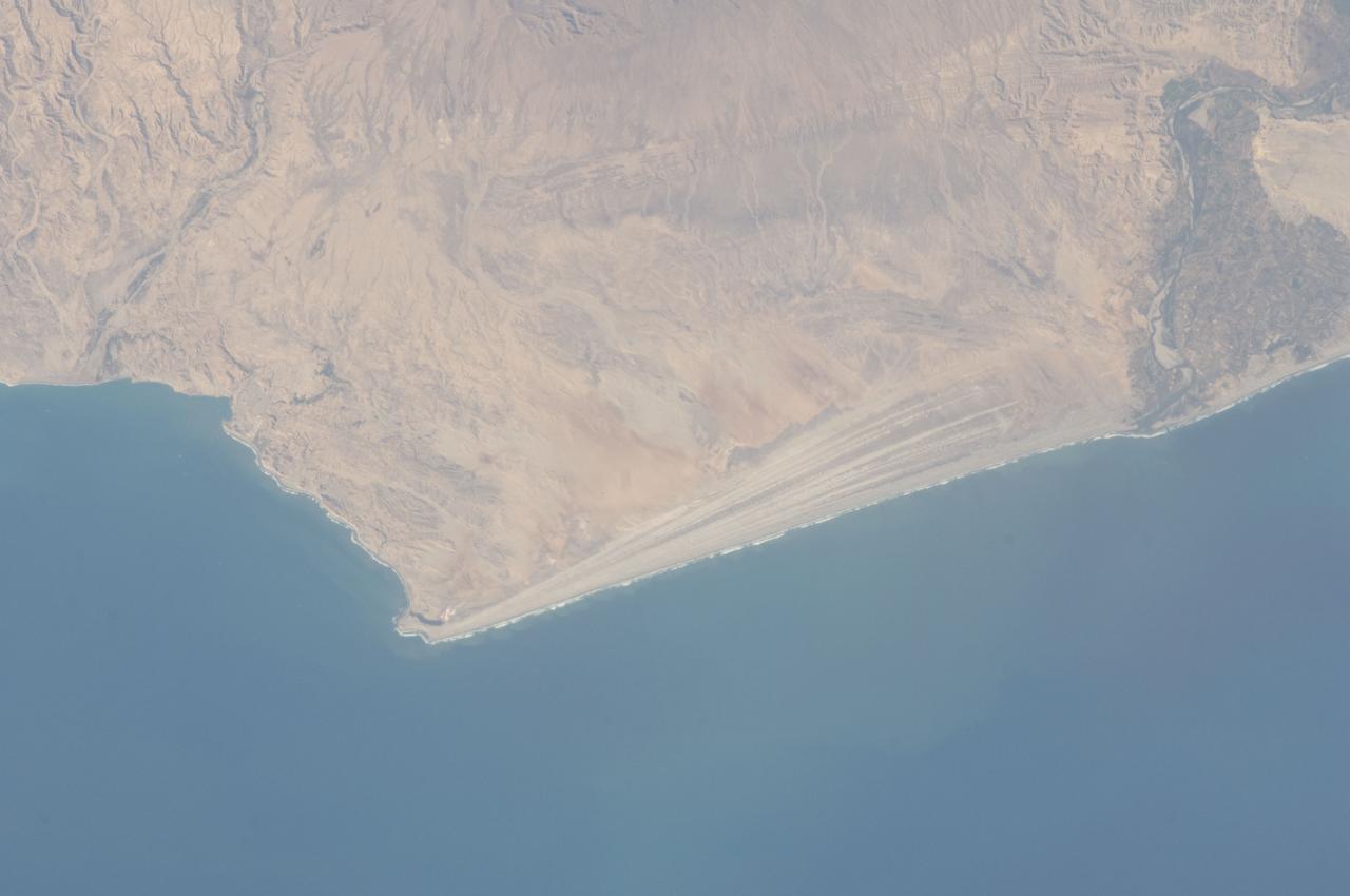 ISS032-E-016579 (11 Aug. 2012) --- A strandplain on coastal Peru is featured in this image photographed by an Expedition 32 crew member on the International Space Station. The scale and orientation of landscape features that are difficult to see on the ground often become readily visible from orbit. Numerous subparallel lines (center) along the arid, northern coast of Peru (about five degrees south of the Equator) are close-packed beach ridges, known collectively as a strandplain (for scale, the strandplain is 30 kilometers long). Each ridge shows the position of a prior shoreline. The Chira River delta appears at right, with dark green agricultural fields occupying the delta of the river. A smaller river reaches the sea, without forming a delta, at extreme left. The prominent cape at lower left is Punta Balcones, a region with many oil wells. Strandplains are built by successive additions of beach sand usually from some nearby source. Currents on this coast of South America come from the south, suggesting to scientists that the Chira River delta (right) is the source of the sand. The newest beach is being formed today by the waves?which appear as the thin ragged white line along the strandplain?supplied by the north-flowing current. The regularity of the spacing of the beaches suggests that some episodic influx of sediment controls beach formation. This influx may be determined by floods coming down the Chira River, possibly controlled by the heavy rains of El Nino events which occur irregularly every few years. Two other sets of faint parallel lines can be seen on higher ground inland (between arrows, center and top right), the upper set stretching all the way from the Chira river floodplain. Seen in many places along the coast of Peru, scientists believe these may also be strandplains (i.e. formed at sea level) generated when the land surface was at a lower altitude; both also may have been produced by sand from the Chira River. The land surface is known to be rising along this coast with the rise of the Andes Mts. (outside the top of the image), explaining why the upper shorelines now lie 120 meters above sea level.