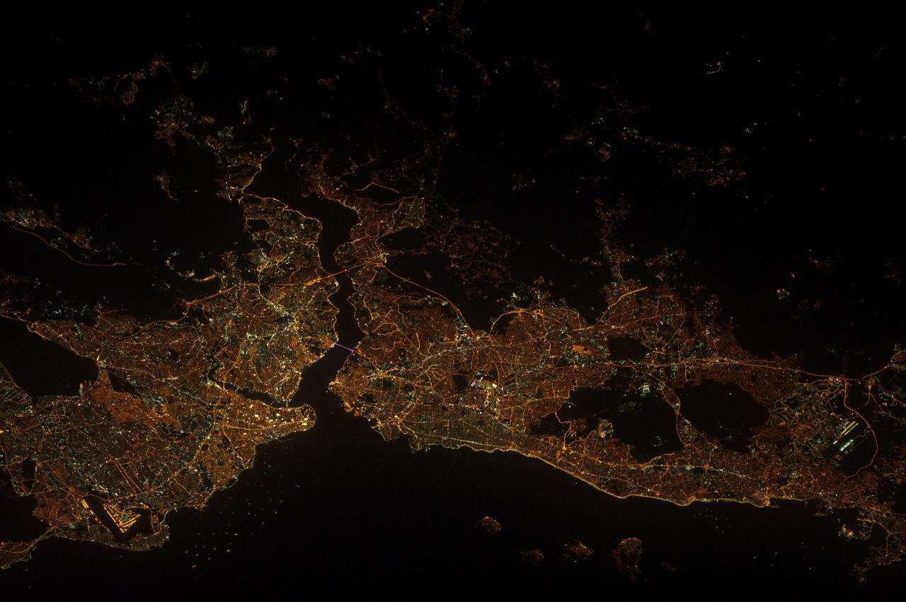 ISS032-E-017547 (9 Aug. 2012) --- A nighttime view of Istanbul, Turkey is featured in this image photographed by an Expedition 32 crew member on the International Space Station. Most of Istanbul?s Asian suburbs (right) appear in this night view from the space station, but only about half the area of the city on the European side (left) can be seen. The margins of the metropolitan area are clearly visible at night, more so than in daylight images. The Bosporus strait (also spelled Bosphorus) (center left) famously separates the two halves of the city, and links the small Sea of Marmara (and the Mediterranean Sea to its south) to the Black Sea (indistinguishable in this night view, top right). The strait is 31 kilometers long, most of which is visible in this view. The Bosporus is a very busy waterway, with larger ships passing to and from the Black Sea competing with numerous ferries that cross between the two halves of the city. Apart from the dark Sea of Marmara (lower margin of the image), the other large dark areas are all wooded hills which provide open spaces for the densely populated city of Istanbul ? one of the largest in Europe with 13.5 million inhabitants. The old city occupies the prominent point at the entrance to the strait. Major traffic arteries are the brighter lines crossing the metropolitan area, and also mark all the shorelines. The First Bosporus Bridge and Second Bridge (also known as the Fatih Sultan Mehmet Bridge) can be seen spanning the strait. The brilliant lights of both international airports serving the region also stand out at lower left and lower right.
