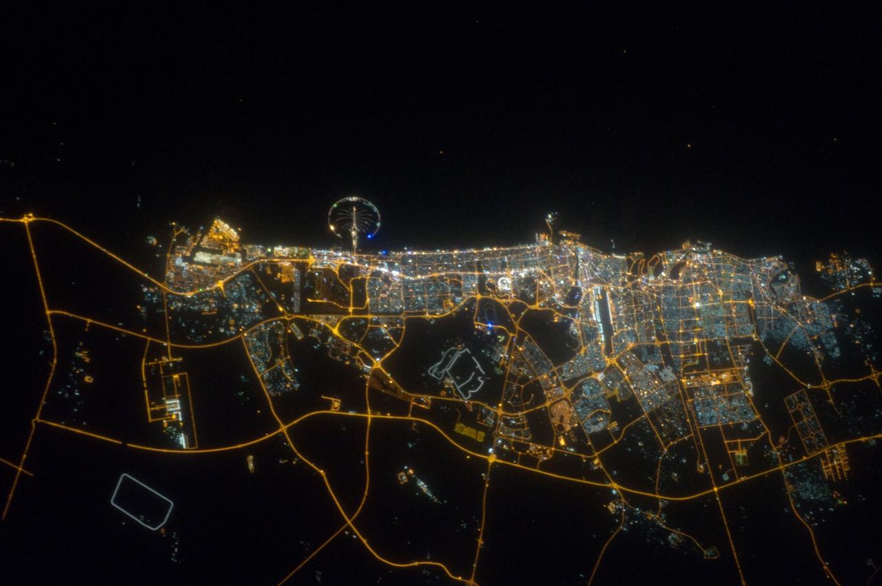 ISS032-E-023718 (11 Aug. 2012) --- The city of Dubai, United Arab Emirates, is featured in this night view photographed by an Expedition 32 crew member on the International Space Station. The city of Dubai is the largest metropolitan area in the emirate of Dubai, one of the member states of the United Arab Emirates. Dubai is located along the southern Persian Gulf on the Arabian Peninsula, and its signature city is known for high profile architectural and development projects. Among the most notable is the Palm Island Resort, a manmade peninsula and surrounding islands built from over 50 million cubic meters of sand. Two other island projects (out of frame), one similar to the Palm Island Resort and another crafted to look like a map of the world, are also visible in other space station imagery along the Dubai coastline.  Orange sodium vapor lights trace out the major highways and surface street grid in and around the metropolitan area, while grey-white mercury vapor lamps fill in the commercial and residential areas. The lighted islands and peninsula of the Palm Island Resort are clearly visible along the coastline. An interesting spiral pattern of lights on the southeastern fringe of the urban area is a camel racetrack. Night time images like this are useful to climate modelers, urban planners, and geographers as they allow for simple definition of urban (densely lit) and rural (sparsely lit) areas.