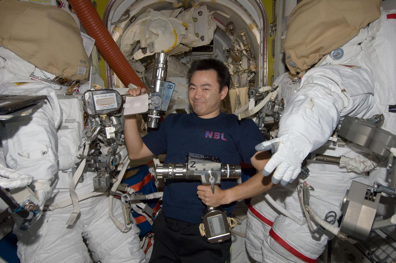 ISS032-E-024569 (29 Aug. 2012) --- Japan Aerospace Exploration Agency astronaut Aki Hoshide, Expedition 32 flight engineer, holding spacewalk tools, is pictured between two Extravehicular Mobility Unit (EMU) spacesuits in the Quest airlock of the International Space Station.