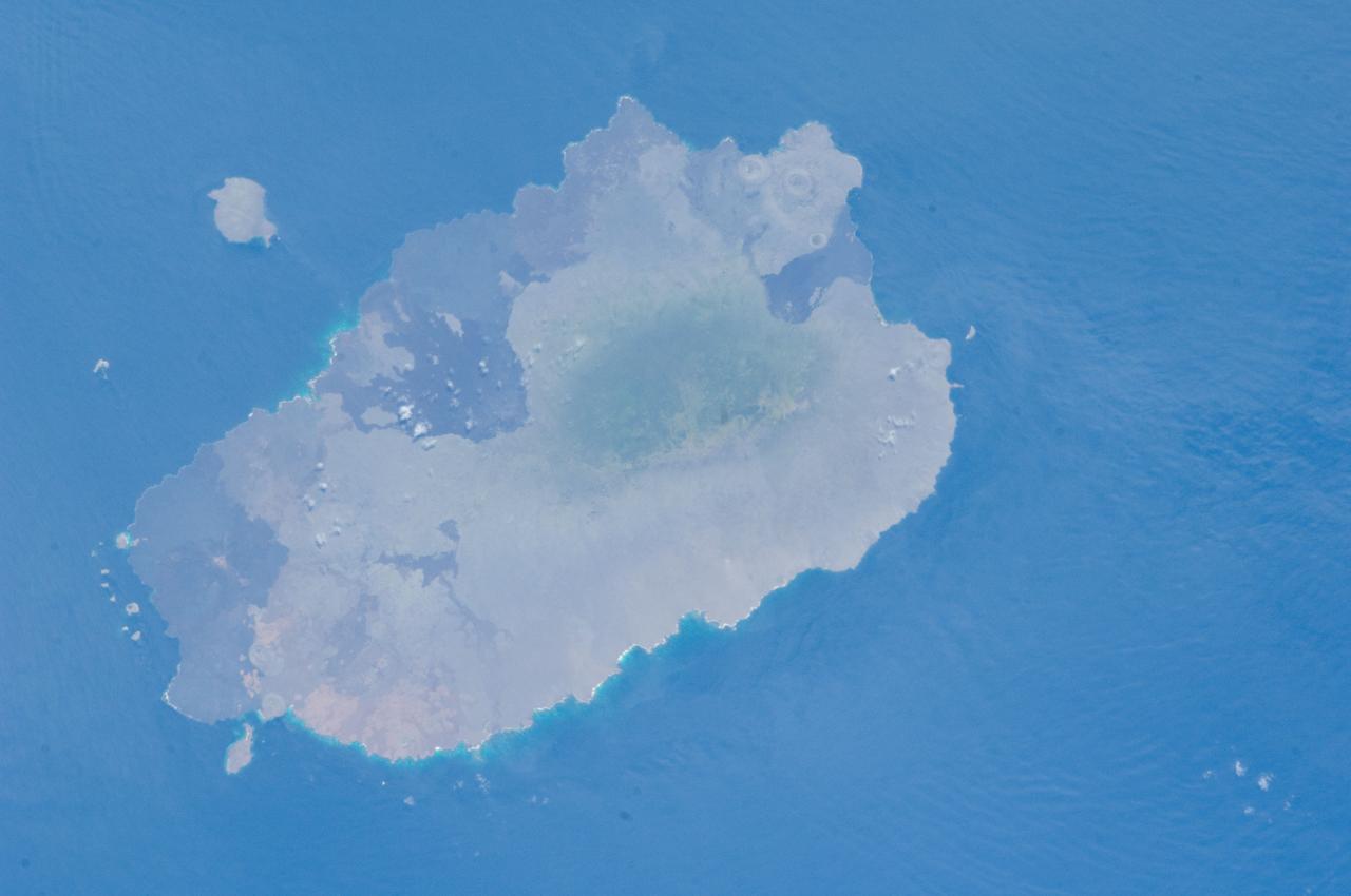 ISS033-E-012648 (18 Oct. 2012) --- Isla Santiago is featured in this image photographed by an Expedition 33 crew member on the International Space Station. The island of Santiago is located near the center of the Galapagos Islands off the coast of Ecuador. The Galapagos Islands are situated near the equator, and were formed from volcanism related to a large mantle plume (also known as a hot spot). This hot spot is very close to the tectonic boundary between the Galapagos Ridge, a plate boundary that is also an oceanic spreading center, and the Nazca and Cocos plates. This combination of mantle plumes and tectonic plate movements produces a unique geological environment, including underwater ridges of volcanoes that influence the water circulation around the Galapagos. All of these aspects contribute to the geology and biology of the Galapagos. Isla Santiago itself is formed from a shield volcano also called Santiago. This type of volcanic structure is recognized by low, flat summits surrounded by extensive flow fields of lava; the lava is not very viscous, so it can flow for great distances from the source vents. Several dark lava flow fields are visible in this photograph, the largest along the eastern, western, and southern coastlines. The small Isla Rabida to the south of Isla Santiago is the peak of another, mostly submerged shield volcano. In addition to the lava flows, other volcanic features known as tuff cones are visible on the eastern and western sides of the island. These cones are formed from the rapid interaction of hot flowing lava and water. The water underneath the lava flow flashes to steam explosively, and this both fragments the lava and rapidly cools it, leading to the formation of cones of glassy, relatively fine-grained volcanic material. The most recent volcanic activity on Isla Santiago occurred during 1904 – 1906. The summit ridge of the Santiago shield volcano is located in the northwestern part of the island (center). Also at center is a large but isolated region of green vegetation primarily located on the south-facing slope below the summit ridge. This image was taken during the dry, or garua, season that lasts from June to November. The season is dominated by cooler air transported by the Southeast Trade winds and cooler waters from the Humboldt and Cromwell currents. The combination of cool air and water results in rain falling only in the island highlands, with south- and east-facing slopes receiving the most precipitation. Despite the favorable topographic location, the yellow green color of the vegetation may indicate water (or other) stress.