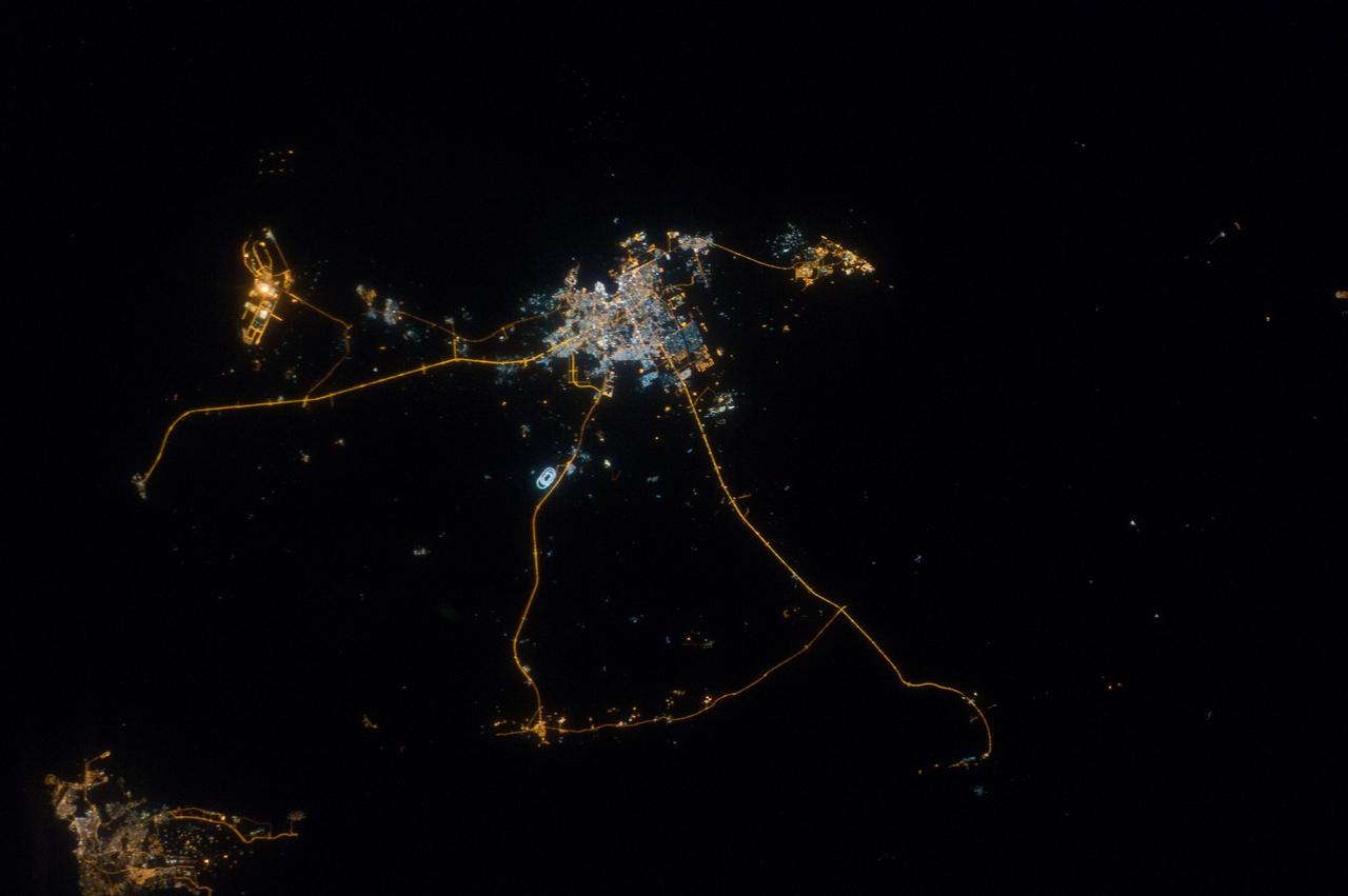 ISS033-E-014856 (13 Oct. 2012) --- A nighttime view of Qatar is featured in this image photographed by an Expedition 33 crew member on the International Space Station. Night lights can be very revealing regarding the distribution of people on the landscape. Here the lights of Qatar show the precise demographic geography of the country. The brightest group at center shows the capital city Doha with the neighboring smaller ports of Ad-Dahira and Umm Sa?id to the north and south, respectively. Even highways and their relative importance can be discerned. Highways are clearly visible leading from the capital west to the Dukhan oil fields, to Saudi Arabia, and to the north of the country--where, judging by the lack of night lights, the population is very low. The relatively low-traffic coast road between the oil fields and the Saudi frontier also stands out. This kind of highly informative human geographic detail is very difficult to discern in daylight images, in which even larger cities, especially in deserts, are hard to see. Almost the entire island nation of Bahrain appears at lower left, with its capital city Manama nearly as bright as the lights of Doha. The difference in light intensity reflects a difference in population?Doha has 1.45 million inhabitants, while the very dense Manama metro area has a population of 1.2 million. While some night views are highly informative about a landscape, they can also be difficult and confusing to identify. Astronauts learn to recognize where they are at night by flying over populated places repeatedly, even though coastlines?one of their best geographic indicators?are generally lost to view because water surfaces and unpopulated land surfaces look the same without illumination (such as from a full moon). Thus the thumb-shaped Qatari peninsula, so well-known in Middle Eastern geography, cannot be discerned at all in this night image. The inset at top right overlays the coastline as seen in daylight onto the night patterns of the image. It shows the Qatari peninsula, with the long arm of the Gulf of Bahrain separating it from Saudi Arabia.