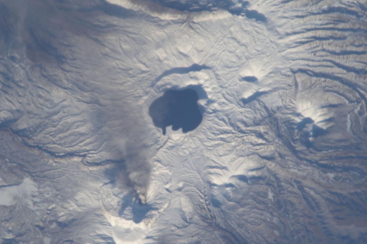 ISS033-E-019822 (9 Nov. 2012) --- An eruption plume from the Karymsky volcano on the Kamchatka Peninsula in the Russian Federation is visible in this image photographed by an Expedition 33 crew member on the International Space Station. The Karymsky stratovolcano stands 1,536 meters above sea level, with most eruptions and occasional lava flows originating from the summit. Karymsky is the most active of Kamchatka’s eastern volcanoes, with almost constant (on a geologic time scale) volcanism occurring since at least the late 18th century when the historical record for the region begins. In light of the high levels of volcanic activity on the Kamchatka Peninsula, the Kamchatka Volcanic Eruption Response Team (KVERT) monitors the activity levels of several volcanoes and issues updates including aviation alerts and webcams. KVERT reported moderate seismic activity at Karymsky during 2-9 Nov. 2012; such activity can indicate movement of magma beneath or within a volcanic structure and can indicate that an eruption is imminent. The Tokyo Volcanic Ash Advisory Center (VAAC) subsequently reported an explosive eruption at Karymsky on Nov. 9, 2012 at 22:15 GMT. This photograph of the resulting ash plume was taken approximately one hour and 35 minutes after the eruption began. The plume extends from the summit of Karymsky (bottom center) to the southeast, with brown ash deposits darkening the snow cover below the plume. The Akademia Nauk caldera – now filled with water to form the present-day Karymsky Lake - is located to the south of Karymsky volcano. Calderas are formed by explosive eruption and emptying of a volcano’s magma chamber – leading to collapse of the structure to form a large crater-like depression. Akademia Nauk last erupted in 1996.