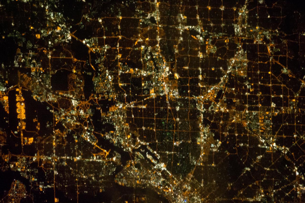 ISS033-E-021663 (15 Nov. 2012) --- A nighttime view of the Dallas, Texas metropolitan area is featured in this image photographed by an Expedition 33 crew member on the International Space Station. Most metropolitan areas of the western United States are configured over large areas with a regular street grid pattern that is highly recognizable from space, particularly at night. The northern Dallas metropolitan area exhibits this pattern. The north-south and east-west grid pattern of major surface streets is highlighted by orange street lighting, lending a fishnet-like appearance to the urban area. Within this framework, smaller residential and commercial buildings and streets give green-gray stipple patterns to some blocks. The airplane terminals of Dallas-Fort Worth International Airport are lit with golden-yellow lights, and surrounded by relatively dark runways and fields at left. Likewise, the runways of Dallas Love Field at lower center are recognizable by their darkness. Other dark areas within the metro region are open space, parks, and water bodies. Dallas is part of the larger Dallas-Fort Worth-Arlington Metropolitan Statistical Area (population 6,526,548 in 2011) as recognized by the U.S. Census Bureau; to most Texans, it is simply ?DFW? or ?the Metroplex.? Several of the larger urban areas within DFW are visible in this image; Dallas, Garland and Richardson all have populations above 100,000 according to the North Central Texas Council of Governments. While historically the economy of Dallas was based in the oil and cotton industries, today commerce, technology, healthcare, and transportation are the major economic drivers.