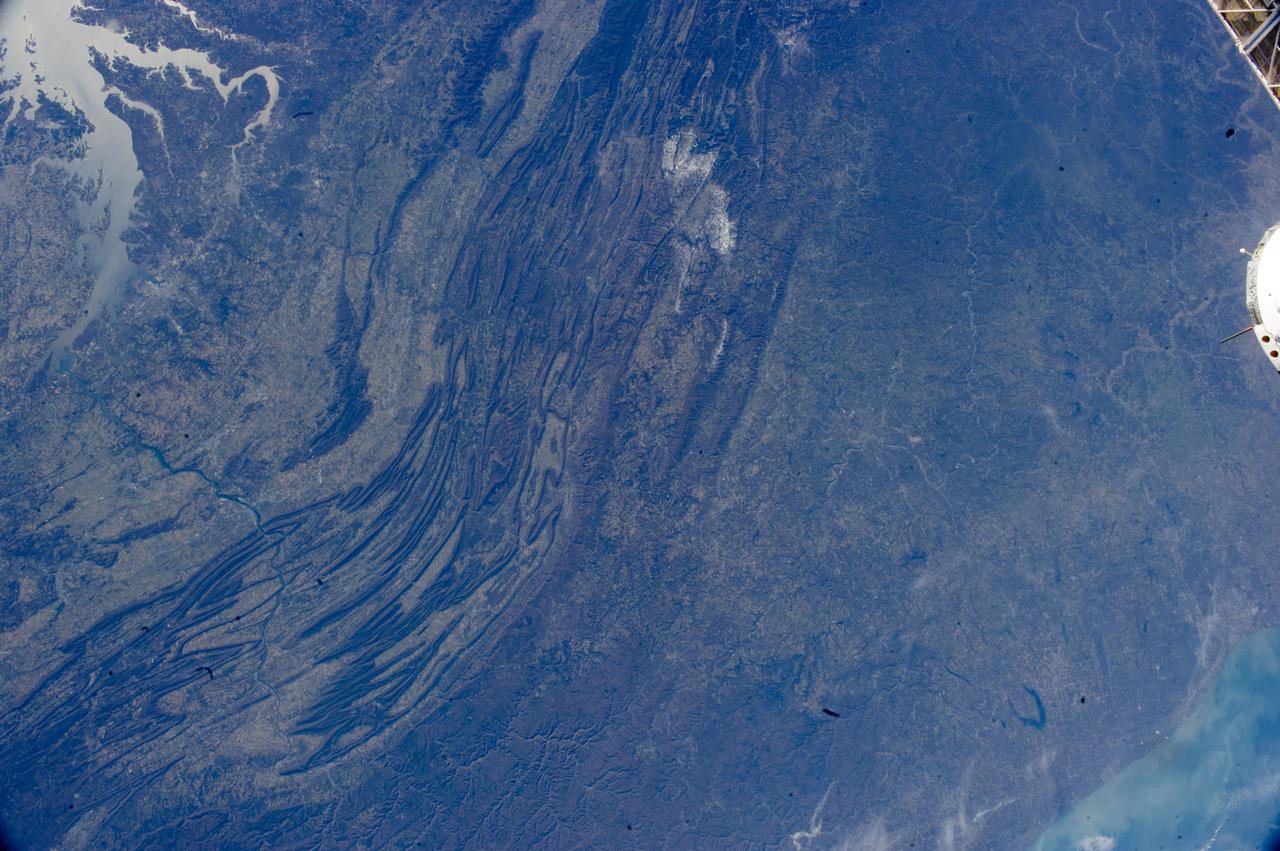 ISS033-E-022378 (17 Nov. 2012) --- The Appalachian Mountains in the eastern Unites States are featured in this image photographed by an Expedition 33 crew member on the International Space Station. This regional view shows the striking visual effect of the valley-and-ridge topography of the Appalachian Mountains as viewed from orbit. The view shows more than 300 miles (500 kilometers) of this low mountain chain, from northeast Pennsylvania (lower left) to southern West Virginia, where a dusting of snow can be seen (top center). Sunglint reflections reveal detail of Chesapeake Bay and the great bend of the Potomac River. Cities are difficult to detect from space during daylight hours, so the sickle-shaped bend of the river is a good visual guide for station crew members trying to photograph the nation?s capital, Washington D.C. (upper left). The farm-dominated Piedmont Plateau is the light-toned area between the mountains and the bay. The Appalachian Mountains appear striped because the ridges are forested; providing a dense and dark canopy cover, while the valleys are farmed with crops that generally appear as lighter-toned areas. Geologically the valleys are the softer, more erodible rock layers, much the preferred places for human settlement. Not only do the larger rivers occupy the valley floors, but all the larger rivers flow in them, soils are thicker, slopes are gentle, and valleys are better protected from winter winds. According to scientists, rocks that form the valley-and-ridge province, as it is known, are relatively old (540-300 million years old), and were laid down in horizontal layers when North America was attached to Europe as the ancient supercontinent of Laurasia.  During this time Gondwanaland ? an ancient supercontinent that included present-day Africa, India, South America, Australia and Antarctica - was approaching Laurasia under the influence of plate tectonics. The northwest coastline of modern Africa was the section of Gondwanaland that ?bumped up? against modern North America over a long period (320 ? 260 million years ago), according to scientists. The net result of the tectonic collision was the building of a major mountain chain, much higher than the present Appalachian range?in the process of which the flat-lying rock layers were crumpled up into a series of tight folds, at right angles to the advance of Gondwanaland. The collision also formed the singular supercontinent of Pangaea. The scientists say that, over the following 200 million years, Pangaea broke apart; the modern Atlantic Ocean formed; and erosion wore down the high mountains. What is left to see are the coastline of North America, and the eroded stumps of the mountain chain as the relatively low, but visually striking present-day Appalachian Mountains.