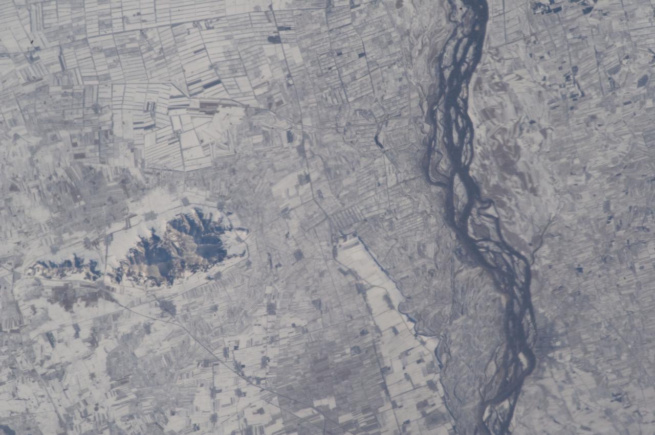 ISS033-E-022759 (18 Nov. 2012) --- Agricultural fields under snow in easternmost China are featured in this image photographed by an Expedition 33 crew member on the International Space Station. This photograph highlights many hundreds of rectangular fields on either side of a 36-kilometer stretch of the braided Songhua River (right). Some fields are easier to see than others due to the winter snow cover. The Songhua joins with the Amur R. about 40 kilometers downstream, at the border with Russia?s Far East. Numerous villages also appear as small gray polygons. Broad floodplains can be recognized on both sides of the river, occupied by fewer fields by almost no villages. The town of Suibing stands out as a larger gray patch on the banks of the river. A significant 300-meter-high hill south of the river throws midmorning shadows (left). The region is one of the most heavily cultivated in northeastern China with corn, soybeans, and sorghum being major crops. The areas of varying whiteness of the snow cover may correlate with zones of different crops and forest cover (for example, on the hill in the center part of the image). The degree to which fallow fields are cleared of vegetation may also affect the apparent snow brightness.