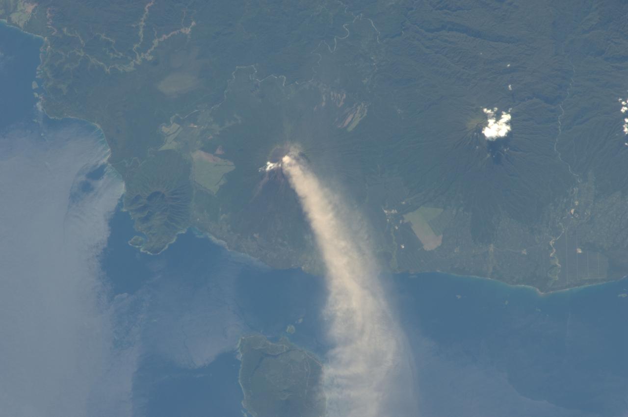 ISS034-E-005496 (30 Nov. 2012) --- An eruption at the Ulawun volcano, New Britain Island, Papua New Guinea is featured in this image photographed by an Expedition 34 crew member on the International Space Station. Numerous volcanoes contribute to the landmass of the island of New Britain, the largest in the Bismarck Archipelago of Papua New Guinea. One of the most active of these volcanoes, Ulawun, is also the highest with a summit elevation of 2,334 meters. This photograph was taken during the most recent phase of volcanic activity at Ulawun. A white steam and ash plume extends from the summit crater of the stratovolcano towards the northwest (center; note the image is oriented such that north is towards the lower left). The plume begins to broaden as it passes the southwestern coast of Lolobau Island approximately 23 kilometers downwind from its source. Ulawun volcano is also known as “the Father”, with the Bamus volcano to the southwest also known as “the South Son”. The summit of Bamus is obscured by white cumulus clouds (not of volcanic origin) in this image. While Ulawun has been active since at least 1700, the most recent eruptive activity at Bamus occurred in the late 19th century. A large region of ocean surface highlighted by sunglint – sunlight reflecting off the water surface, lending it a mirror-like appearance– is visible to the north-northeast of Ulawun (lower left).