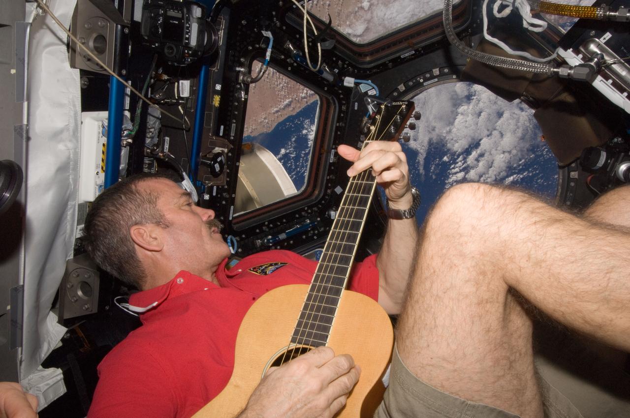 ISS034-E-009799 (25 Dec. 2012) --- Canadian Space Agency astronaut Chris Hadfield strums his guitar in the International Space Station's Cupola on Dec. 25, 2012. Hadfield, a long-time member of an astronaut band called Max Q, later joined with the other five Expedition 34 crew members in a more spacious location to provide an assortment of Christmas carols for the public.