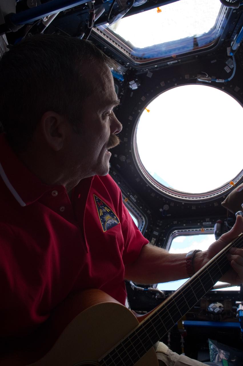 ISS034-E-010295 (25 Dec. 2012) --- Canadian Space Agency astronaut Chris Hadfield strums his guitar in the International Space Station's Cupola on Dec. 25, 2012. Hadfield, a long-time member of an astronaut band called Max Q, later joined with the other five Expedition 34 crew members in a more spacious location to provide an assortment of Christmas carols for the public.
