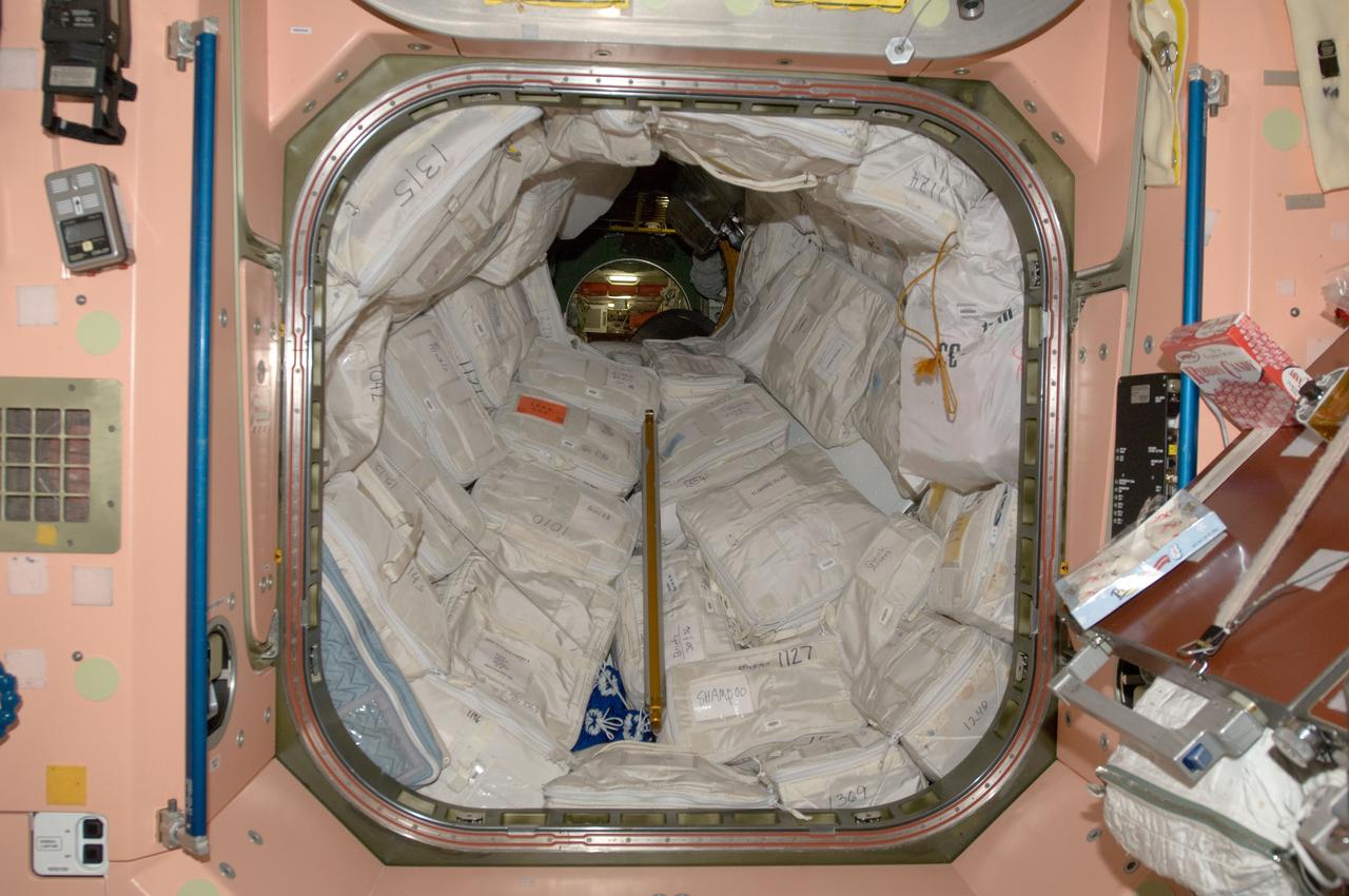 View of stowage in the aft end of the Node 1 and the hatch leading to Pressurized Mating Adapter 1 (PMA1). The PMA1 is also lined with stowed equipment.  Photo was taken during Expedition 34.