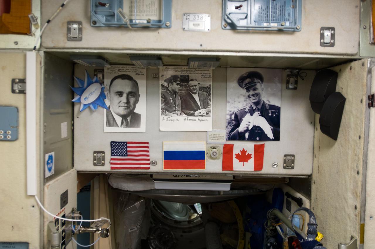 View of Yuri Alexievich Gagarin (first space traveler) photo and other photos,above Service Module (SM) hatch.  The blue and white rosette on the left with the writing Ð¿Ð¾ÑÐ° Ð² ÐºÐ¾ÑÐ¼Ð¾Ñ is the symbol and name of the Russian television program for children that covers cosmonautic and International Space Station (ISS) topics.  Photo was taken during Expedition 34.