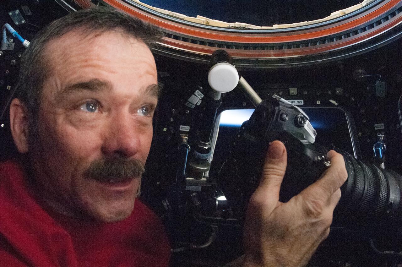 ISS034-E-024095 (7 Jan. 2013) --- Canadian Space Agency astronaut Chris Hadfield, Expedition 34 flight engineer, holds a still camera while looking through a window in the Cupola of the International Space Station.