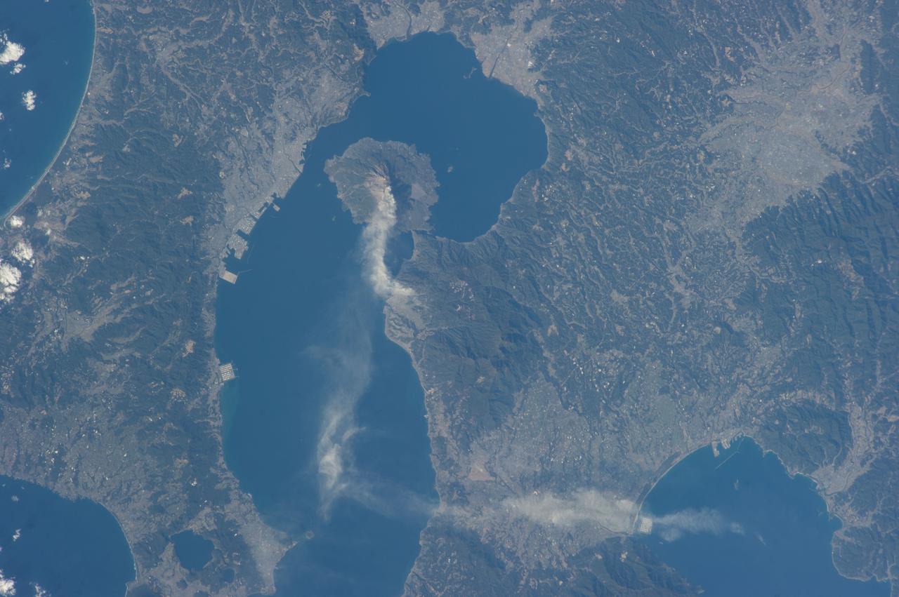 ISS034-E-027139 (10 Jan. 2013) --- Sakurajima Volcano in Kyushu, Japan is featured in this image photographed by an Expedition 34 crew member on the International Space Station. This photograph highlights Sakurajima, one of Japan’s most active volcanoes (center). There are several eruption craters near the 1,117 meter summit of Sakurajima; according to scientists, Kita-dake to the north last erupted approximately 5,000 years ago, while Minami-dake and Showa crater to the south have been the site of frequent eruptions since at least the 8th century. The ash plume visible near the volcano summit and extending to the southeast may have originated from either Minami-dake or Showa craters. Scientists believe that Sakurajima began forming approximately 13,000 years ago; prior to 1914, the volcano was an island in Kagoshima Bay—it was joined to the mainland by volcanic material following a major eruption in 1914. The image highlights the proximity of several large urban areas (Aira, Kagoshima, Kanoya, Kirishima, and Miyakonojo are readily visible) to Sakurajima. This has prompted studies of potential health hazards presented by the volcanic ash (Hillman et al. 2012), which are particularly important if more powerful explosive eruptive activity resumes at the volcano. The Tokyo Volcanic Ash Advisory Center (VAAC) of the Japan Meteorological Agency issues advisories when eruptions occur. An advisory on the activity captured in this image was issued less than one hour before the crew member took the photograph, by which time the plume tail had encountered northeast-trending upper-level winds (bottom center).