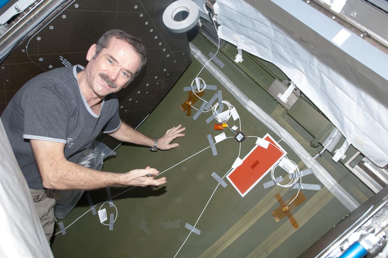 View of Canadian Space Agency (CSA) Chris Hadfield,Expedition 34 Flight Engineer (FE),installing Ultra-Sonic Background Noise Tests (UBNT) sensors behind rack in the U.S. Laboratory using the International Space Station (ISS) as Testbed for Analog Research (ISTAR) procedures.  These sensors detect high frequency noise levels generated by ISS hardware and equipment operating within the U.S. Laboratory.  Photo was taken during Expedition 34.