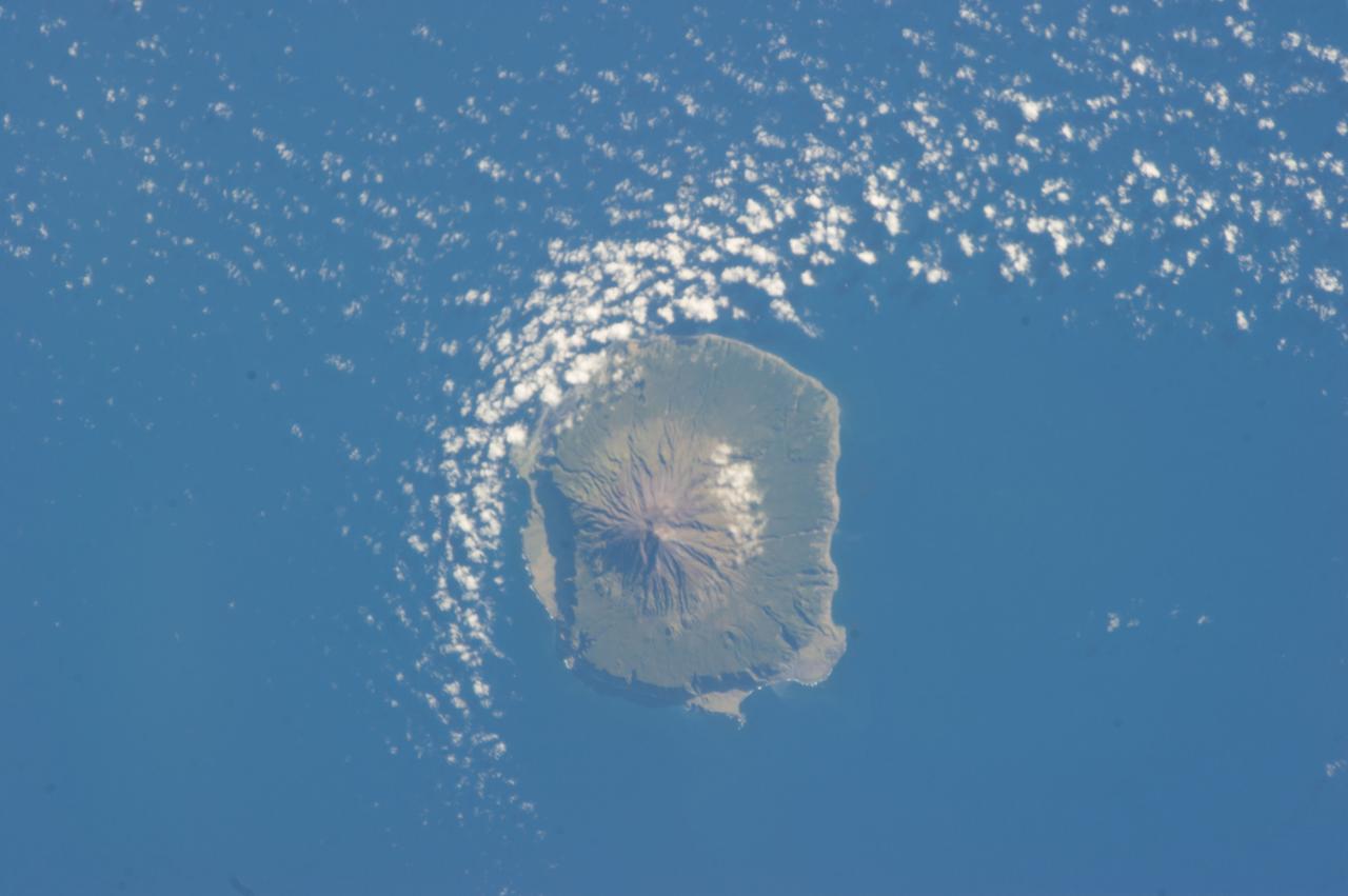 ISS034-E-041528 (6 Feb. 2013) --- Tristan da Cunha is featured in this image photographed by an Expedition 34 crew member on the International Space Station. The island is located in the southern Atlantic Ocean; more than 3,700 kilometers from the northern coastline of Antarctica, approximately 2,800 kilometers to the southern tip of Africa, and more than 3,000 kilometers from the eastern coastline of South America. The island forms part of the British Overseas Territory of Saint Helena, Ascension, and Tristan da Cunha. The shoreline of the 13-kilometer-wide island is marked on most sides by steep cliffs, with lower beach areas on the southern and north-northwestern sides. The island is notable for its bird population, including important breeding grounds for a variety of petrels, albatrosses, penguins and shearwaters. Tristan da Cunha is a shield volcano; a type of volcanic structure usually recognized by a low, broad profile and composed of silica-poor lavas (such as basalt). The upper surface of this low base appears dark green in this photograph. Steeper, brown to tan colored slopes mark the central cone of the volcano at the island?s center. The summit crater, Queen Mary?s Peak, sits at an elevation of 2,060 meters above sea level. While geologic evidence indicates that eruptions have occurred from the central crater, lavas have also erupted from flank vents along the sides of the volcano as well as smaller cinder cones. The last known eruption of Tristan da Cunha took place 1961-1962 and forced evacuation of the only settlement on the island, Edinburgh of the Seven Seas. The settlement is located along the northern coastline of the island (obscured by clouds in this image). This is considered to be the most remote permanent settlement on Earth, with its citizen?s nearest neighbors located 2,173 kilometers to the northeast on the island of St. Helena.