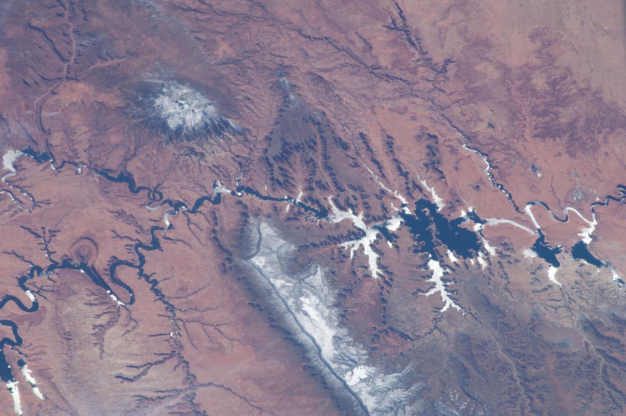 ISS034-E-066804 (12 March 2013) --- One of the Expedition 34 crew members aboard the Earth-orbiting International Space Station on March 12 , 2013 photographed this image of the Colorado Plateau, which spans northern Arizona, southern Utah, northwestern New Mexico and southwestern Colorado. This physiographic province is well known for its striking landscapes and broad vistas—an impression that is enhanced by the view from the orbital perspective of the space station. The image highlights part of the Utah-Arizona border region of the plateau and includes several prominent landforms. The Colorado River, dammed to form Lake Powell in 1963, crosses from east to west, (which is actually left to right in this image because the view looks toward the south, and north appears toward the bottom of the frame). The confluence of the Colorado and San Juan Rivers is also visible in the image. Sunglint, or sunlight reflected off a water surface back toward the observer, provides a silvery. Mirror-like sheen to some areas of the water surfaces. The geologic uplift of the Colorado Plateau led to rapid down cutting of rivers into the flat sedimentary bedrock, leaving spectacular erosional landforms. One such feature – the Rincon ---preserves evidence of a former meander bend of the Colorado River. Photo credit: NASA