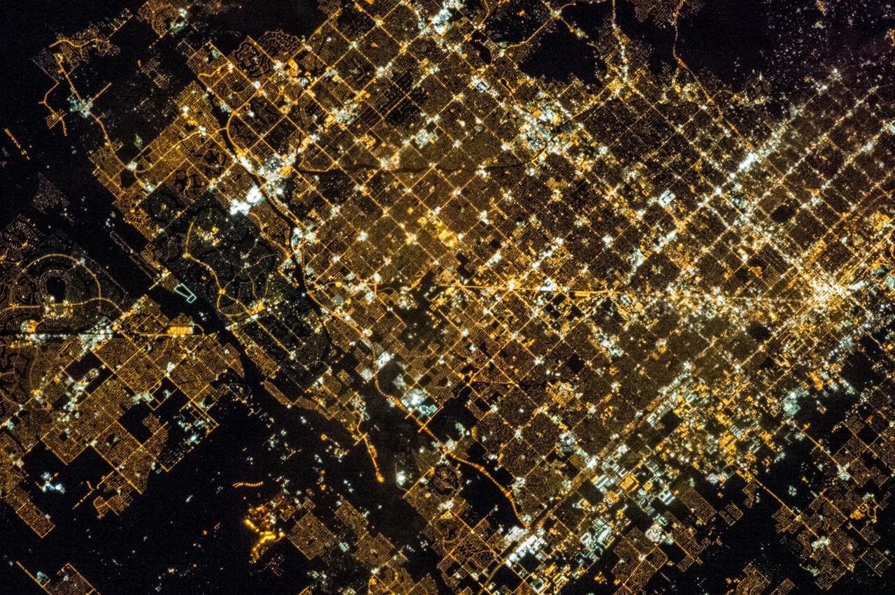 ISS035-E-005438 (16 March 2013) --- One of the Expedition 35 crew members on the International Space Station used a still camera with a 400 millimeter lens to record this nocturnal image of the Phoenix, Arizona area. Like many large urban areas of the central and western United States, the Phoenix metropolitan area is laid out along a regular grid of city blocks and streets. While visible during the day, this grid is most evident at night, when the pattern of street lighting is clearly visible from above – in the case of this photograph, from the low Earth orbit vantage point of the International Space Station. The urban grid form encourages growth of a city outwards along its borders, by providing optimal access to new real estate. Fueled by the adoption of widespread personal automobile use during the 20th century, the Phoenix metropolitan area today includes 25 other municipalities (many of them largely suburban and residential in character) linked by a network of surface streets and freeways. The image area includes parts of several cities in the metropolitan area including Phoenix proper (right), Glendale (center), and Peoria (left). While the major street grid is oriented north-south, the northwest-southeast oriented Grand Avenue cuts across it at image center. Grand Avenue is a major transportation corridor through the western metropolitan area; the lighting patterns of large industrial and commercial properties are visible along its length. Other brightly lit properties include large shopping centers, strip centers, and gas stations which tend to be located at the intersections of north-south and east-west trending streets. While much of the land area highlighted in this image is urbanized, there are several noticeably dark areas. The Phoenix Mountains at upper right are largely public park and recreational land. To the west (image lower left), agricultural fields provide a sharp contrast to the lit streets of neighboring residential developments. The Salt River channel appears as a dark ribbon within the urban grid at lower right.