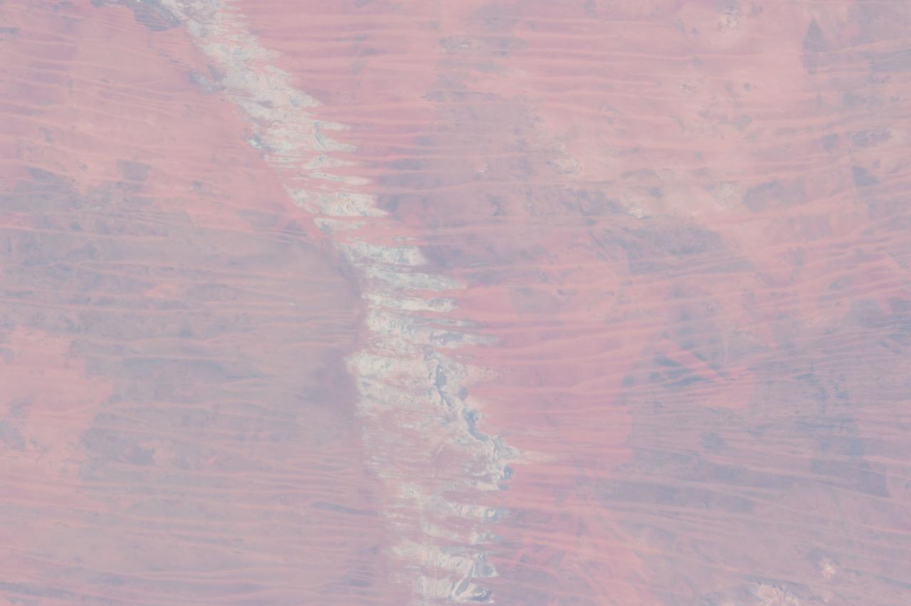ISS035-E-009454 (25 March 2013 ) --- One of the Expedition 35 crew members aboard the Earth-orbiting International Space Station  used a 400 millimeter lens to photograph this view of the Great Sandy Desert, northwestern Australia on March 25.  It bears evidence that much of Australia is arid. In northwest Australia the Great Sandy Desert holds great geological interest as a zone of active sand dune movement; strings of narrow lakes that represent very ancient rivers are also present.  While a variety of dune forms can be seen in the region,  this photograph features numerous linear dunes (approximately 25 meters high) separated in a roughly regular fashion (0.5?1.5 kilometers), and aligned closely to the winds that generated them?that is, winds blowing from east to west.  Where linear dunes converge, dune confluences point downwind. One of the main visual impressions flying over such tropical dune fields ? both from an airplane or from the orbital station outpost?apart from the dune patterns are fire scars where thin vegetation has been burned off the dunes. The result is dunes that appear red from the underlying sand (image top left and top right), and darker areas where the vegetation remains (image lower left and lower right).  The white feature visible down the center of the image is Lake Auld, the white color being the result of a cemented combination of fine clayey sediment and salts from evaporation of flood waters that occasionally fill the lake. Wider views of the area show that this lake is part of what is now known to have been a major, ancient river system in northwest Australia, draining northwest to the Indian Ocean. Such sinuous lakes are also known in Australia as ?river lakes.?  Scientists point out that the river system is remarkably well preserved considering that the rivers were probably active in the Paleocene Epoch more than 55 million years ago.  Australia then lay much further south in a wetter climatic zone. Today?s desert climate results in almost all rivers in the Great Sandy Desert being dry.  Linear dunes can be seen entering Lake Auld on the east side.  During flooding events, the sand of the dune noses is dispersed, becoming incorporated into the lake floor sediments together with muds and salts. During the long intervening dry periods, sand can blow across the lake floor to build thinner, smaller dunes visible as linear accumulations on the west side of the lake.