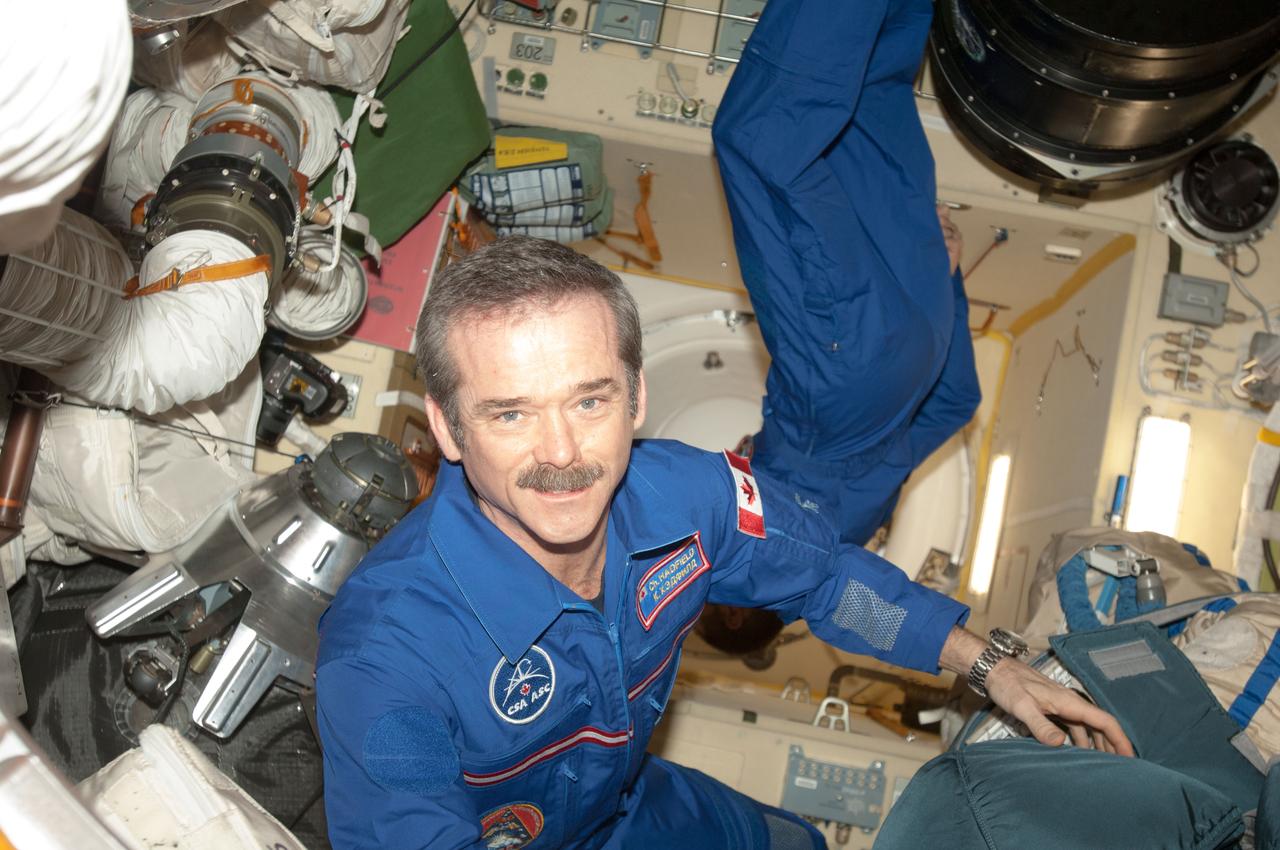 Expedition 35 commander Chris Hadfield and flight engineer Tom Marshburn (partially obscured) are photographed in the Poisk Mini-Research Module 2 (MRM2) during preparations for hatch opening with the docked Soyuz TMA-08M/34S spacecraft. Hadfield is a Canadian Space Agency (CSA) astronaut.