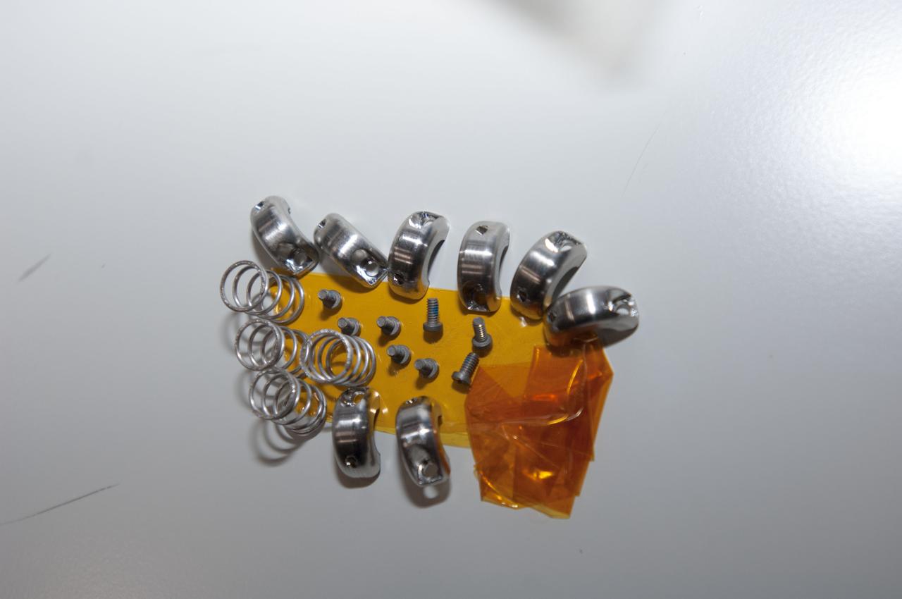 Documentation of retainers, springs and screws used during Expedition 35 Ku Communications (Comm) Unit fastener modifications. Parts are attached to Kapton tape.