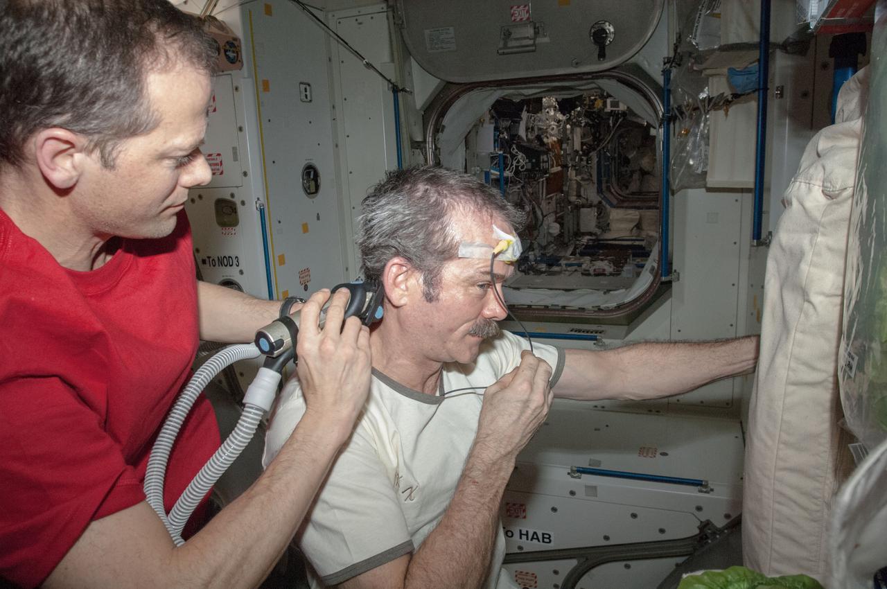 Expedition 35 flight engineer Tom Marshburn gives commander Chris Hadfield a haircut (using clippers attached to a vacuum hose) in the Unity Node 1. Hadfield (a Canadian Space Agency astronaut) has a temperature sensor taped to his forehead.