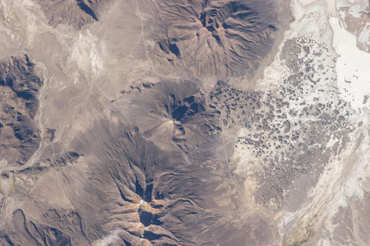 ISS035-E-18006 (8 April 2013) --- One of the Expedition 35 crew members  aboard the Earth-orbiting International Space Station photographed this image of Tata Sabaya Volcano, located in the Altiplano region of Bolivia.  The volcano rises to a summit elevation of 5430 meters above sea level. While its current form is that of a “youthful”  stratovolcano, the regional geological evidence indicates an older, eventful history, according to scientists.  The scientists say that prior to approximately 12,000 years ago (during the late Pleistocene Epoch), a large debris avalanche was formed by collapse of the ancestral Tata Sabaya volcano. Debris from the avalanche swept into the nearby Salar de Coipasa –at that time filled with a lake larger than today – significantly changing its northwestern coastline. Timing of the event is obtained from tufa deposits formed on debris islands during a high stand of the Coipasa lake – illustrating the geological principle of cross-cutting relationships, in that the debris avalanche had to have occurred before the tufa deposits were formed in the lake.  The Tata Sabaya stratovolcano is located at image center. Several young lava flows are visible on the northwestern and western flanks of the volcano. Peaks visible to the northeast and southwest appear to be volcanoes as well, but unlike Tata Sabaya there is no record of recent activity from either of them (according to the Smithsonian National Museum of Natural History’s Global Volcanism Program). As the Altiplano became more arid and the Coipasa Lake shrank, much of the hummocky terrain of the debris avalanche became exposed over an area of more than 300 square kilometers. The hummocky terrain is clearly visible at image right. White salt deposits of the salar surround many of the individual hummocks, making them “islands” once again.