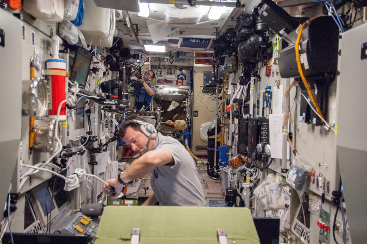 ISS035-E-029752 (26 April 2013) --- Russian cosmonauts Roman Romanenko, foreground, and Alexander Misurkin busy themselves with various chores in the Zvezda service module aboard the Earth-orbiting International Space Station during the rendezvous and docking of the Progress 51 cargo craft.