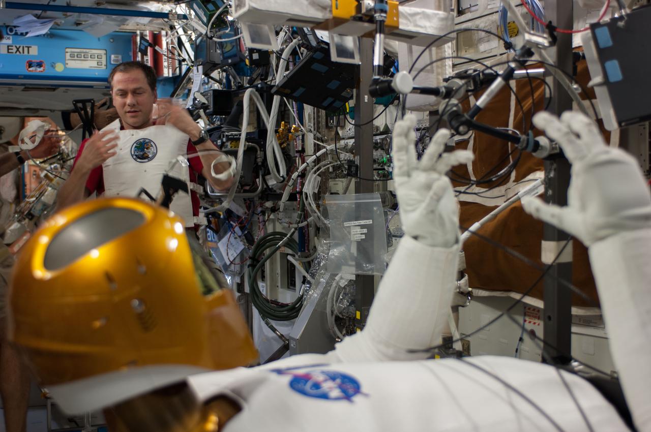 ISS035-E-030794 (25 April 2013) --- NASA astronaut Tom Marshburn (pictured in background), Expedition 35 Flight Engineer, performs the second of a two-day session  of Taskboard and Tele-operations with R 2 onboard the International Space Station. R 2 is the dexterous humanoid robot that was carried up to the station by one of NASA's final shuttle flights in 2011. The goals for these activities were orientation and depth familiarization, individual hand grasp and hand-to-hand object transfer; and all were completed nominally. The Robonaut Tele-operation System is used to demonstrate the ability to effectively control Robonaut from the station. The research objective is to evaluate this control method in terms of its ability to perform tasks as well as measure the time necessary to complete the defined tasks. This capability will need to be developed to support future operations of Robonaut in the space environment as well as certain intravehicular activity situations.