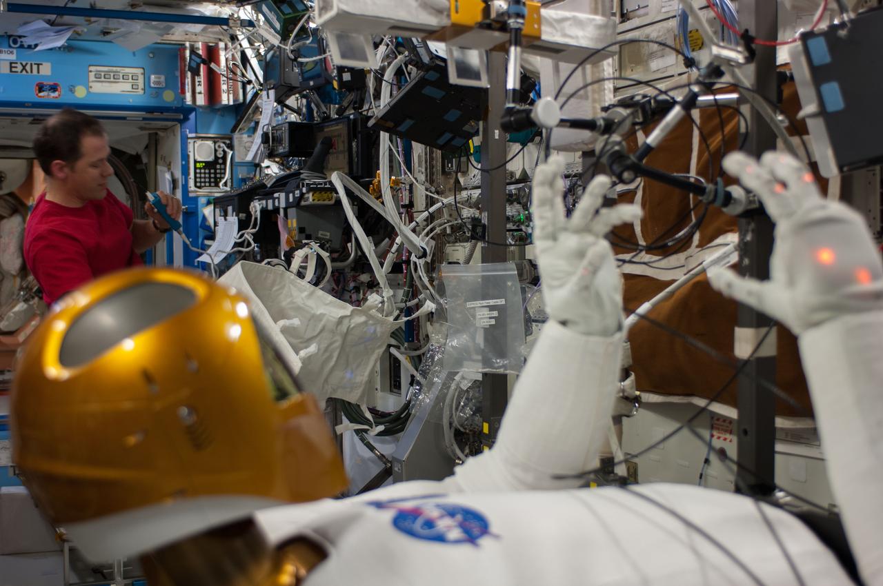 ISS035-E-030794 (25 April 2013) --- NASA astronaut Tom Marshburn (pictured in background), Expedition 35 Flight Engineer, performs the second of a two-day session  of Taskboard and Tele-operations with R 2 onboard the International Space Station. R 2 is the dexterous humanoid robot that was carried up to the station by one of NASA's final shuttle flights in 2011. The goals for these activities were orientation and depth familiarization, individual hand grasp and hand-to-hand object transfer; and all were completed nominally. The Robonaut Tele-operation System is used to demonstrate the ability to effectively control Robonaut from the station. The research objective is to evaluate this control method in terms of its ability to perform tasks as well as measure the time necessary to complete the defined tasks. This capability will need to be developed to support future operations of Robonaut in the space environment as well as certain intravehicular activity situations.