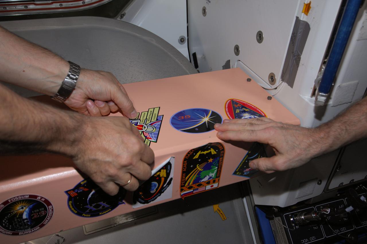 ISS035-E-040104 (13 May 2013) --- One of the final acts aboard the International Space Station following a change of command and prior to a crew departure traditionally has been placement of respective increment logo decals at various places onboard the orbital outpost. Expedition 36 Commander Pavel Vinogradov (mostly out of frame) adds his crew's decal to the many that have been placed over a period of many years in the Unity node.