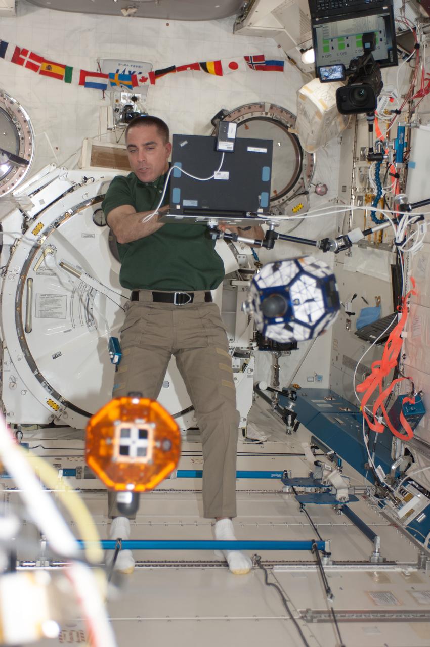 ISS036-E-015549 (5 July 2013) --- In the International Space Station’s Kibo laboratory, NASA astronaut Chris Cassidy, Expedition 36 flight engineer, watches as he devotes some time with the long-running SPHERES experiment, also known as Synchronized Position Hold Engage and Reorient Experimental Satellites. The experiment is run in conjunction with students who program bowling ball-sized satellites using algorithms. The free-floating satellites are programmed to perform maneuvers potentially influencing the design of future missions.