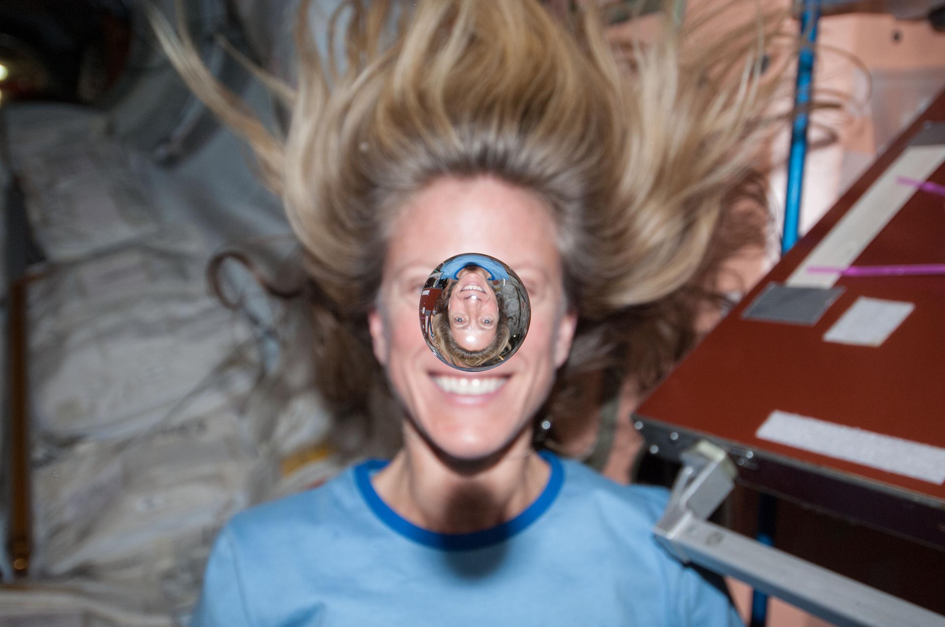 A picture of a female astronaut on the International Space Station with a large droplet of water in front of her face.