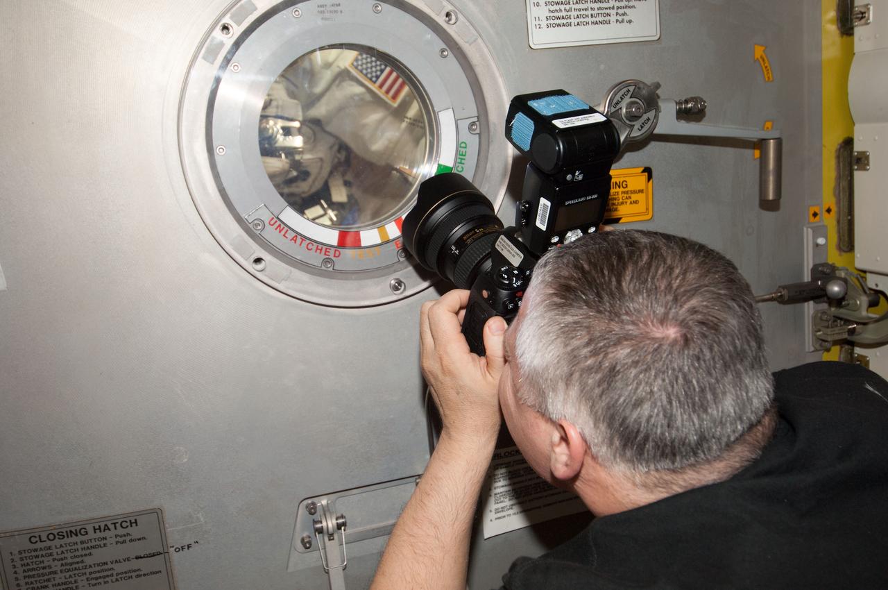 ISS036-E-019889 (16 July 2013) --- Russian cosmonaut Fyodor Yurchikhin, Expedition 36 flight engineer, uses a digital still camera at a hatch window of the International Space Station’s Quest airlock to photograph European Space Agency astronaut Luca Parmitano and NASA astronaut Chris Cassidy as the July 16 spacewalk draws to a close. The spacewalk was ended early due to issues with Parmitano’s spacesuit.