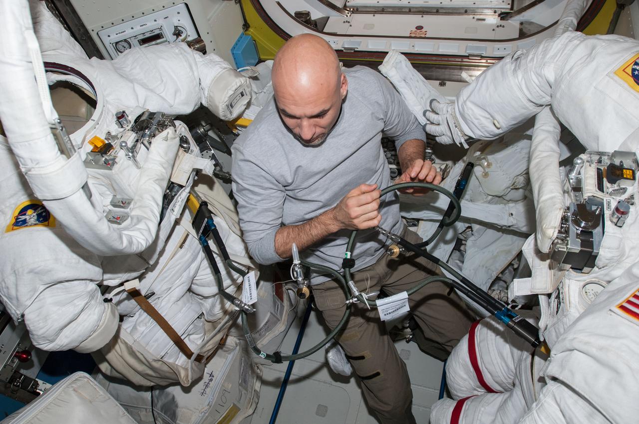ISS036-E-022368 (18 July 2013) --- European Space Agency astronaut Luca Parmitano, Expedition 36 flight engineer, works with spacewalk hardware between two Extravehicular Mobility Unit (EMU) spacesuits in the Quest airlock of the International Space Station.